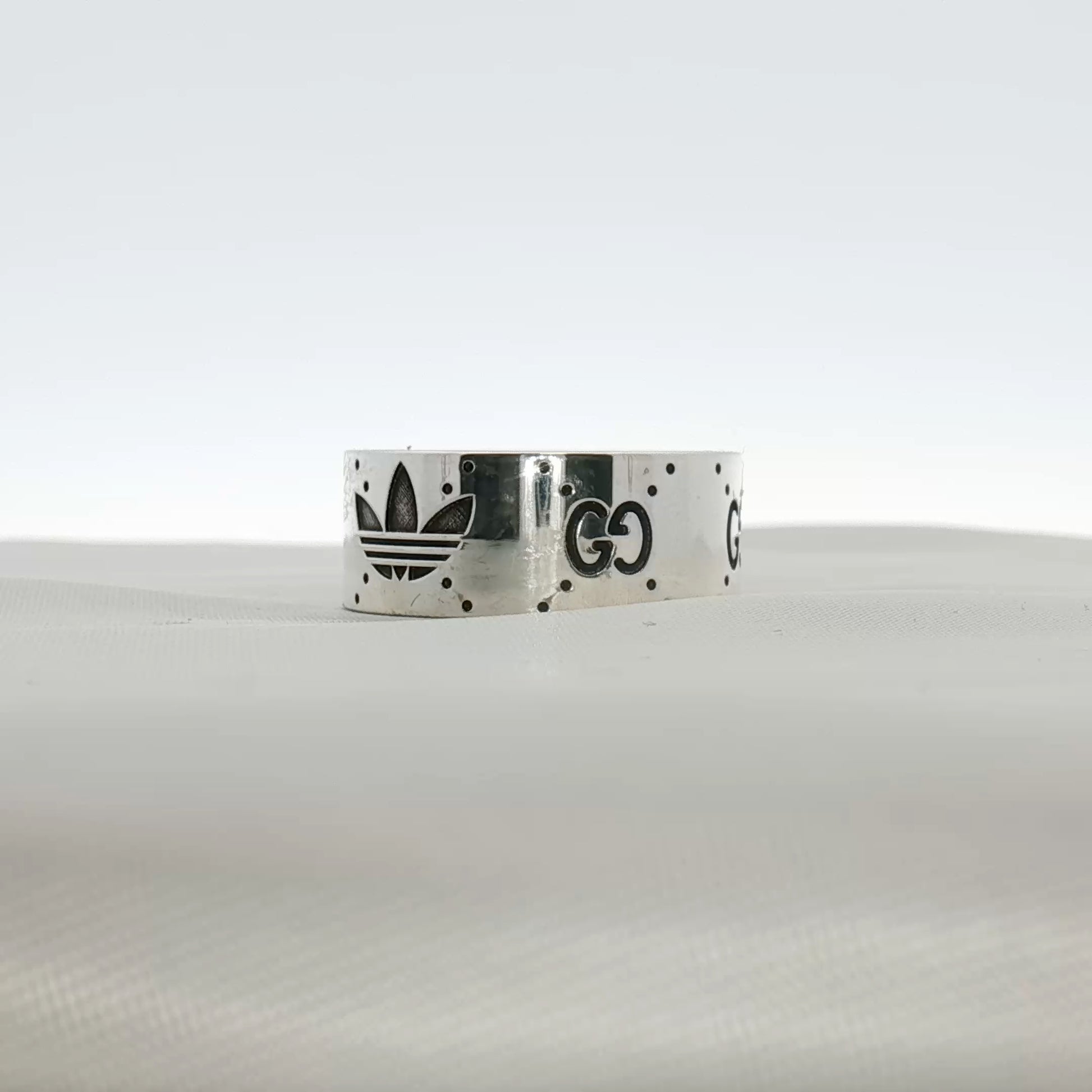 Gucci x Adidas logo band ring in jewelry, featuring a sleek gold and silver design with brand logos engraved.