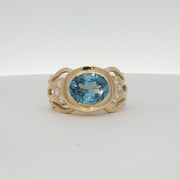 18K yellow gold oval blue gemstone and diamond ring by Gold & Beyond, showcasing a sparkling blue gem with diamond accents.