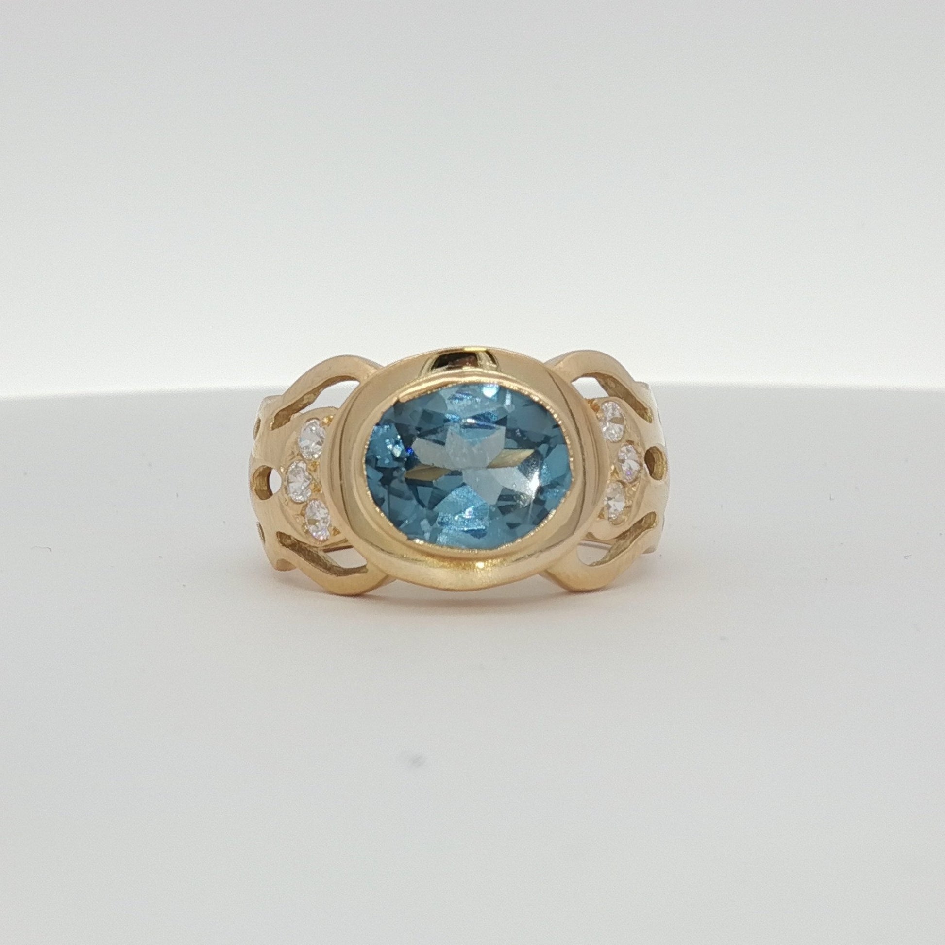 18K yellow gold oval blue gemstone and diamond ring by Gold & Beyond, showcasing a sparkling blue gem with diamond accents.