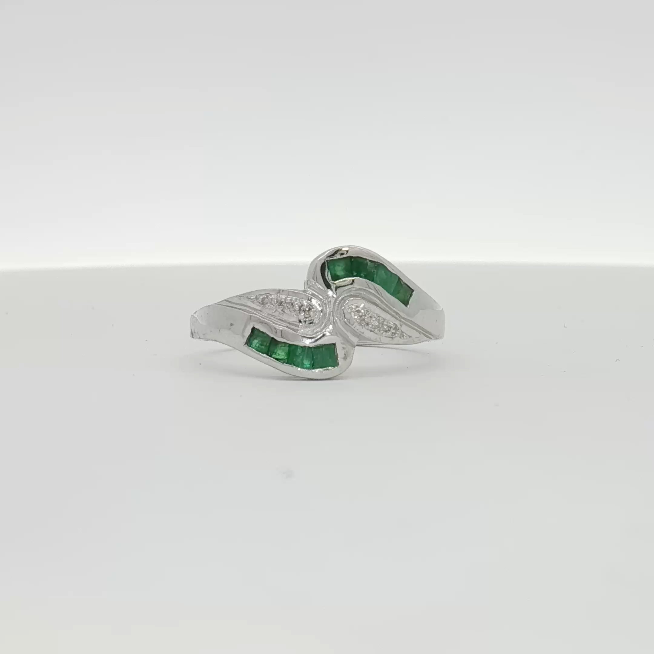 14K white gold emerald and diamond bypass ring featuring sparkling gemstones and a sleek, modern jewelry design.