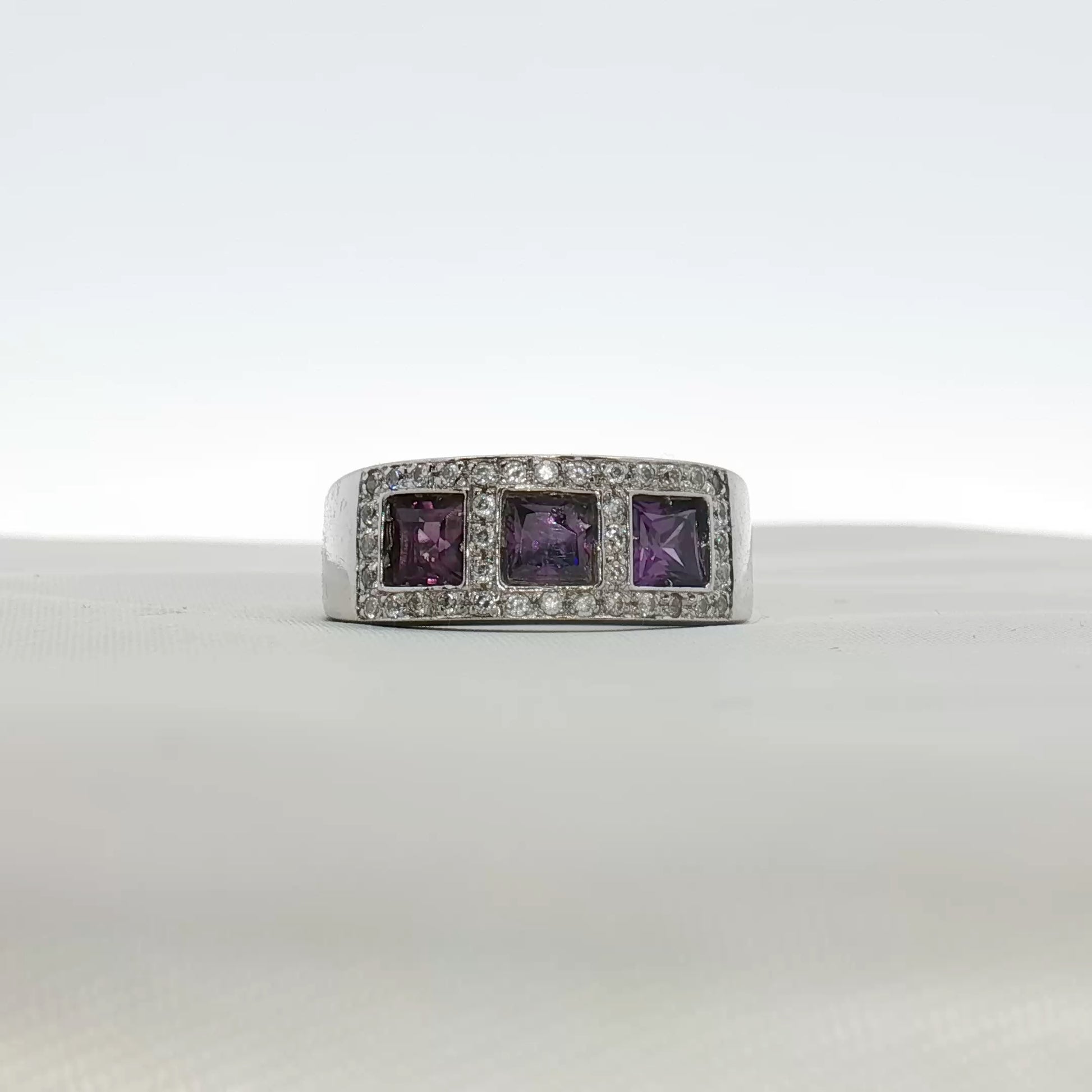 Three-stone diamond and purple gemstone ring by Gold & Beyond, showcasing sparkling diamonds with vibrant purple accents in a jewelry design.