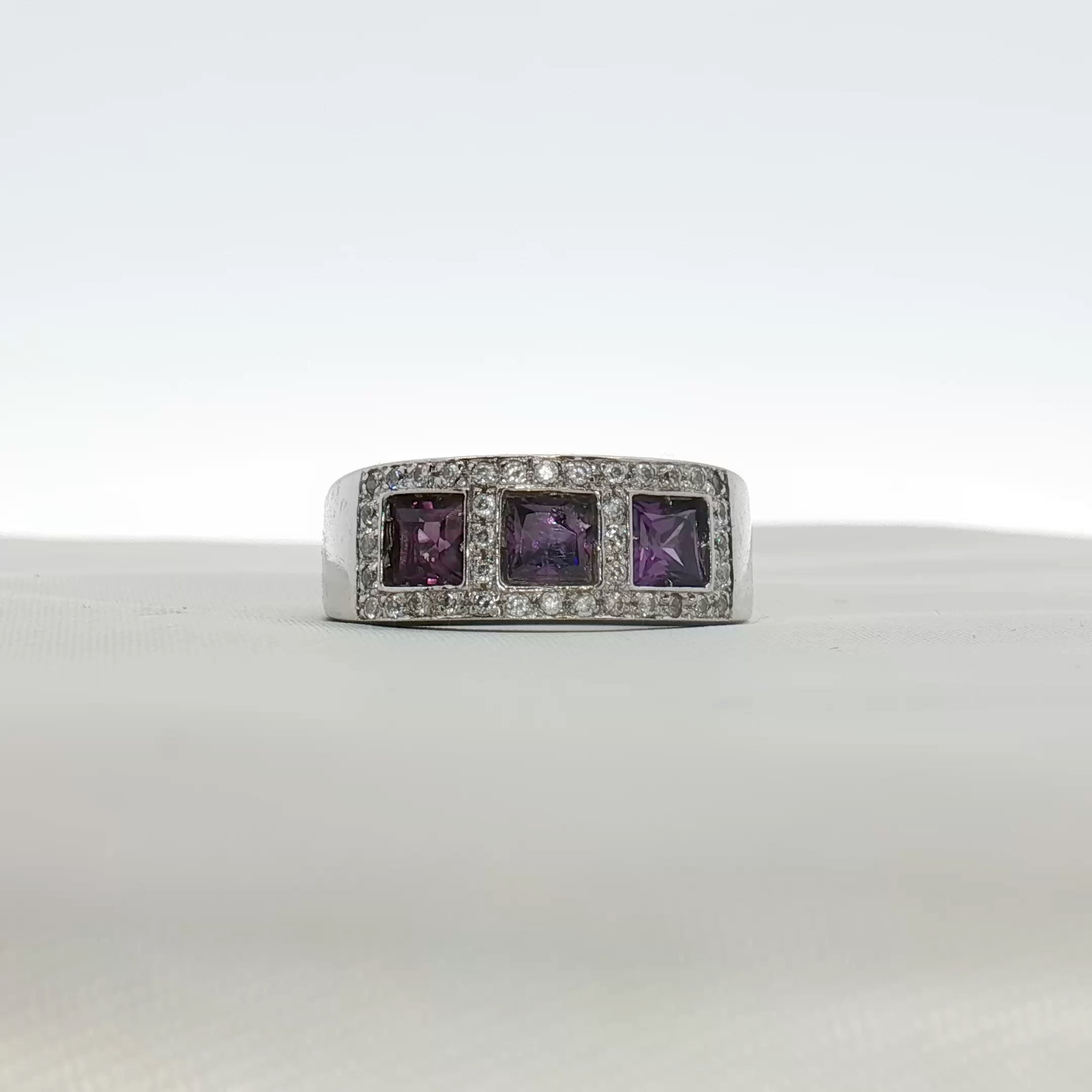 Three-stone diamond and purple gemstone ring by Gold & Beyond, showcasing sparkling diamonds with vibrant purple accents in a jewelry design.