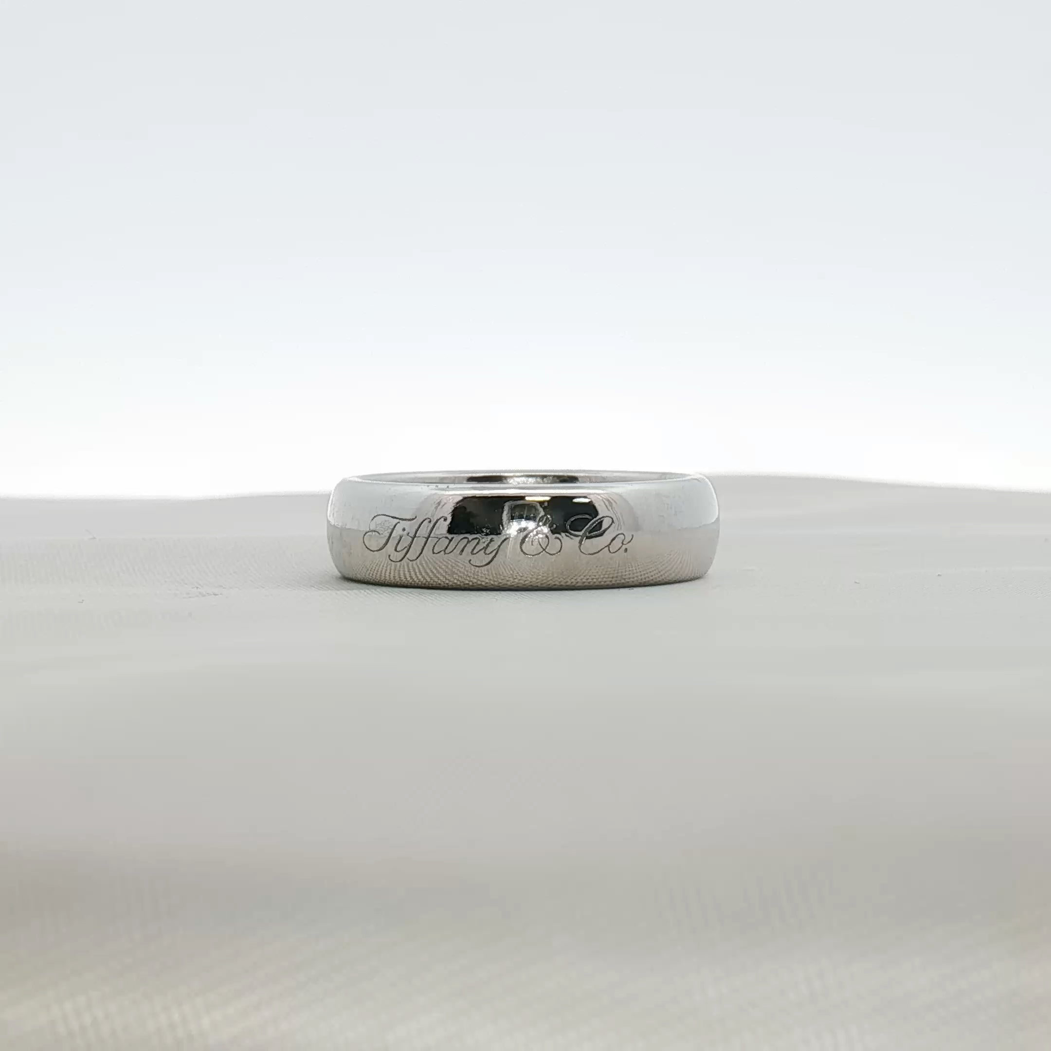 Tiffany & Co. platinum wedding band ring with a sleek, polished design, displayed on a jewelry stand.