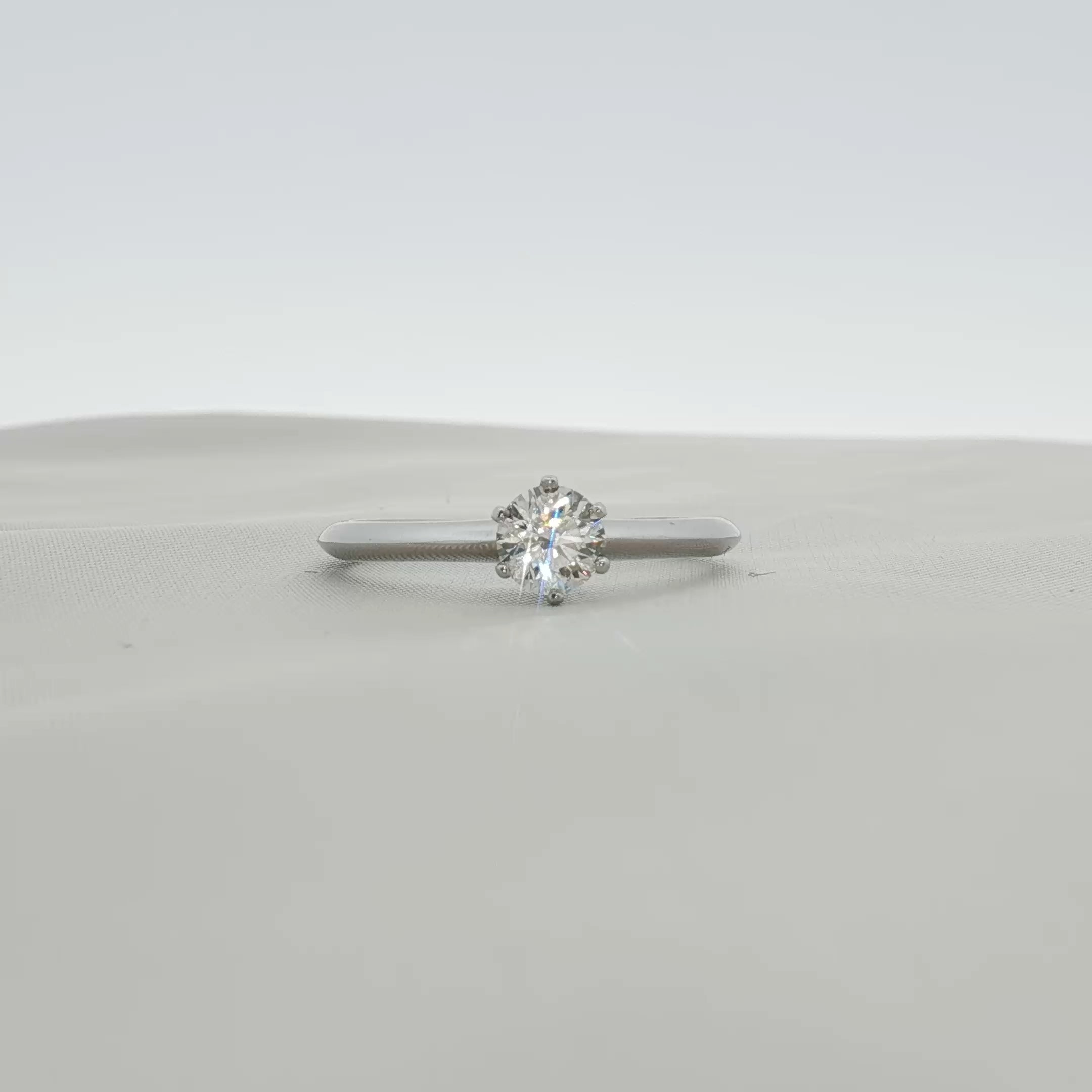 Platinum solitaire engagement ring by Tiffany & Co. featuring a central diamond set on a sleek band, displayed on a jewelry stand.