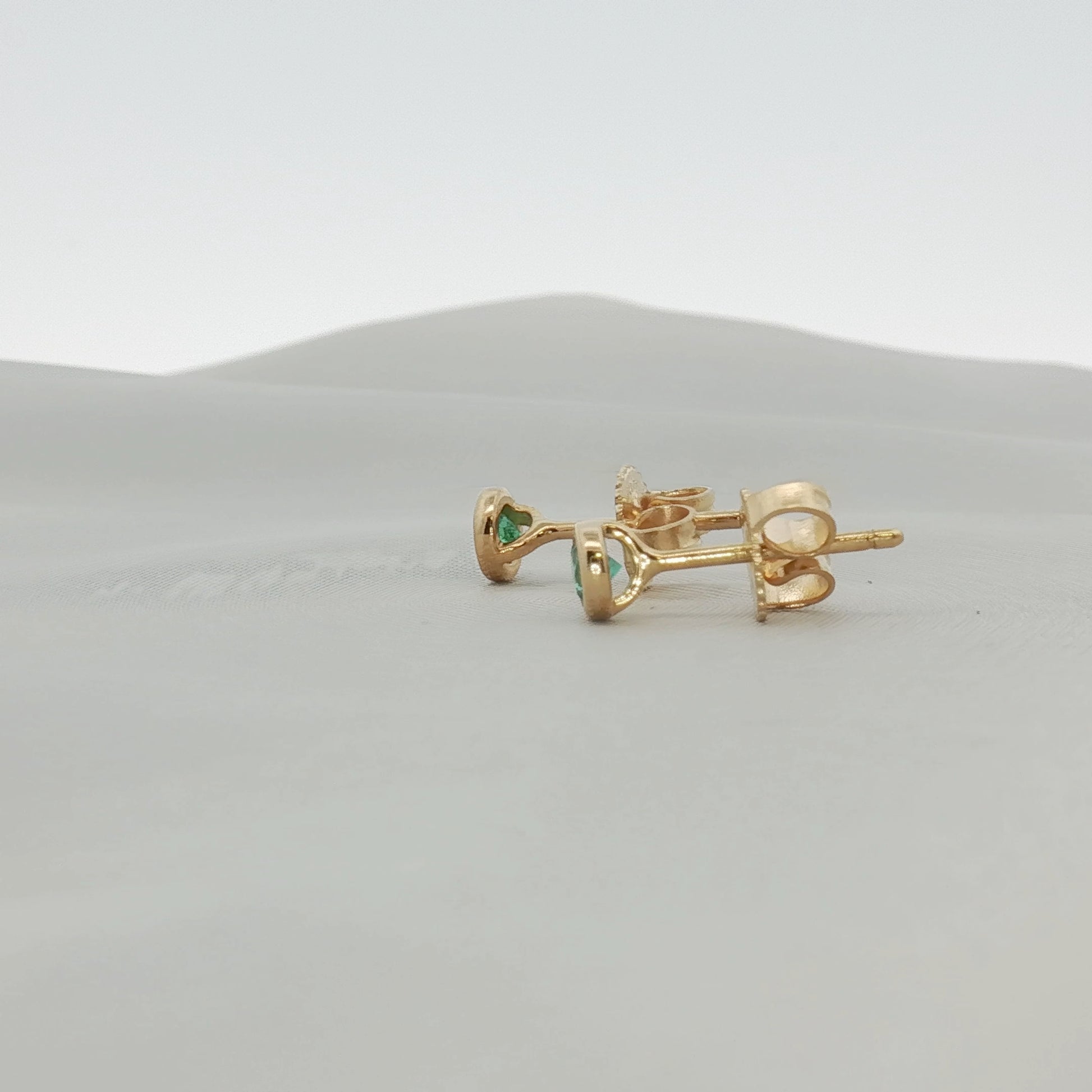 Tiffany & Co. 18K yellow gold emerald stud earrings featuring vibrant green emerald gemstones in a jewelry image.