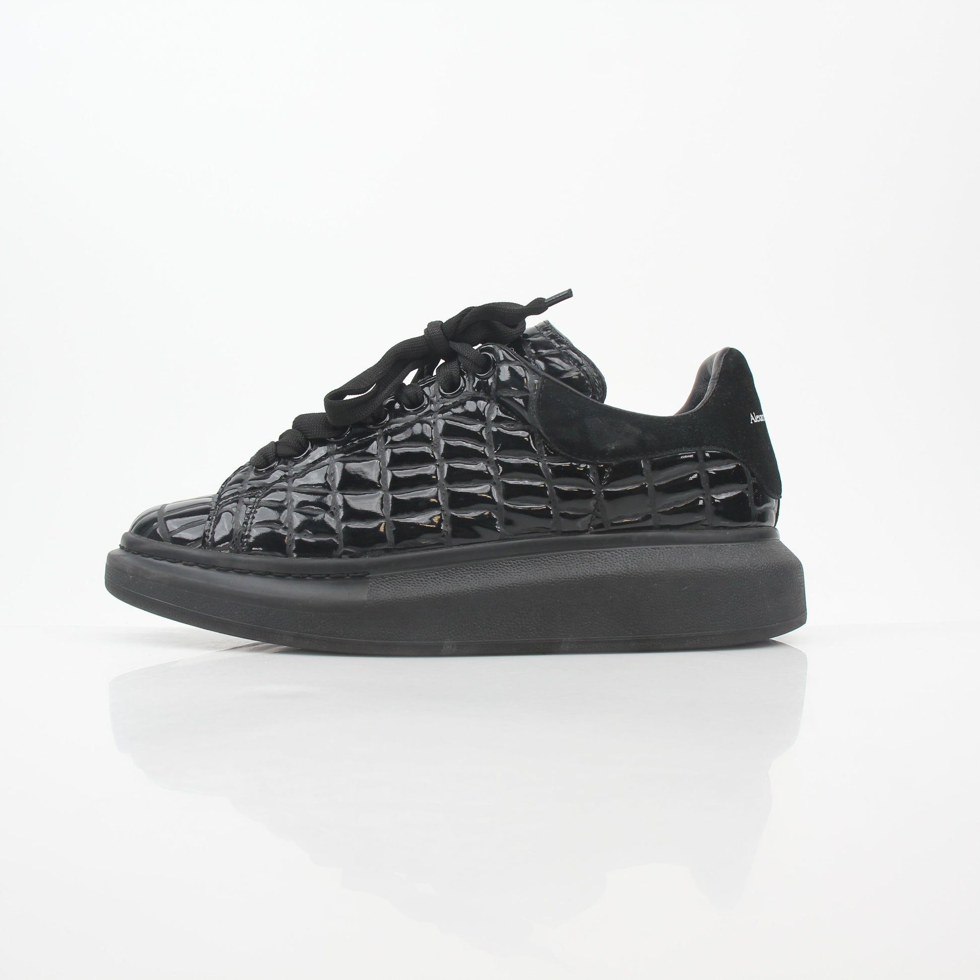 Black croc-embossed Alexander McQueen oversized sneakers with chunky design and white rubber soles, displayed on a plain background.