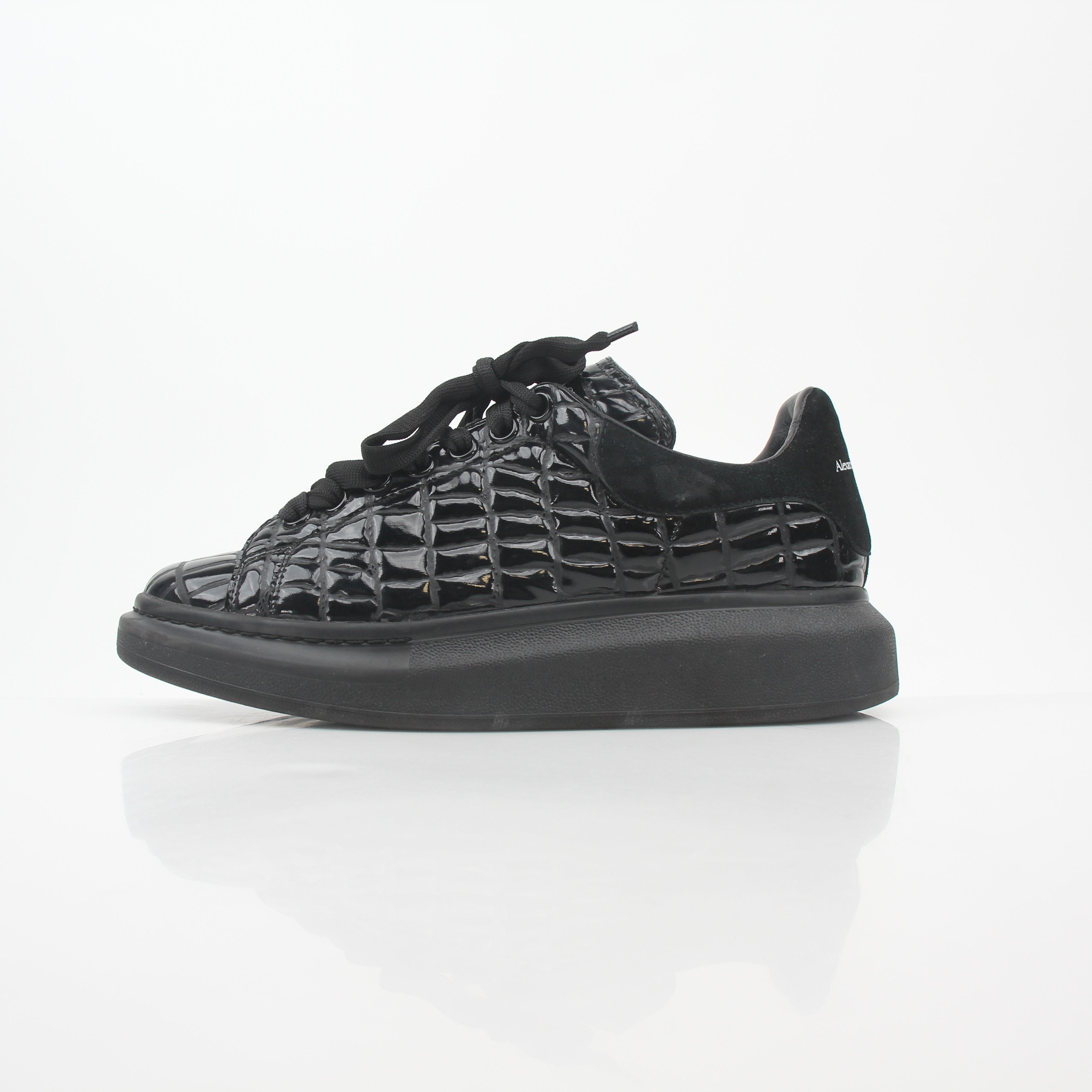 Black croc-embossed Alexander McQueen oversized sneakers with chunky design and white rubber soles, displayed on a plain background.