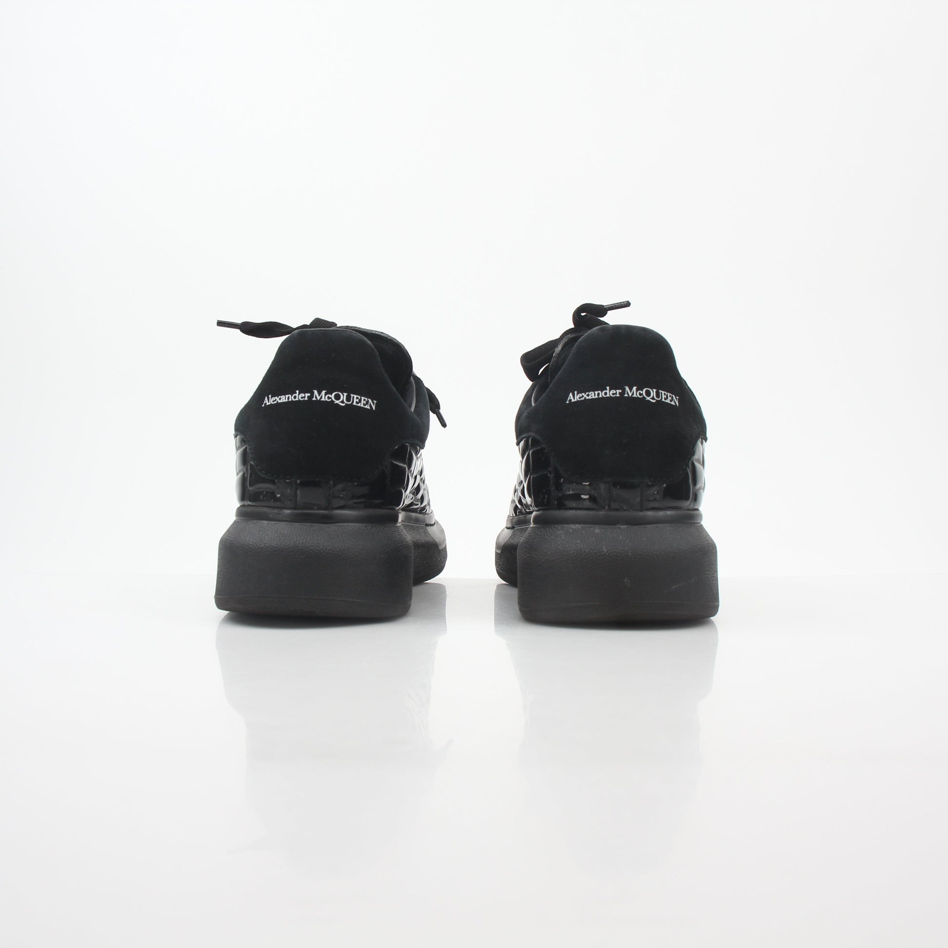 Black croc-embossed Alexander McQueen oversized sneakers with chunky soles, stylishly displayed on a white background.