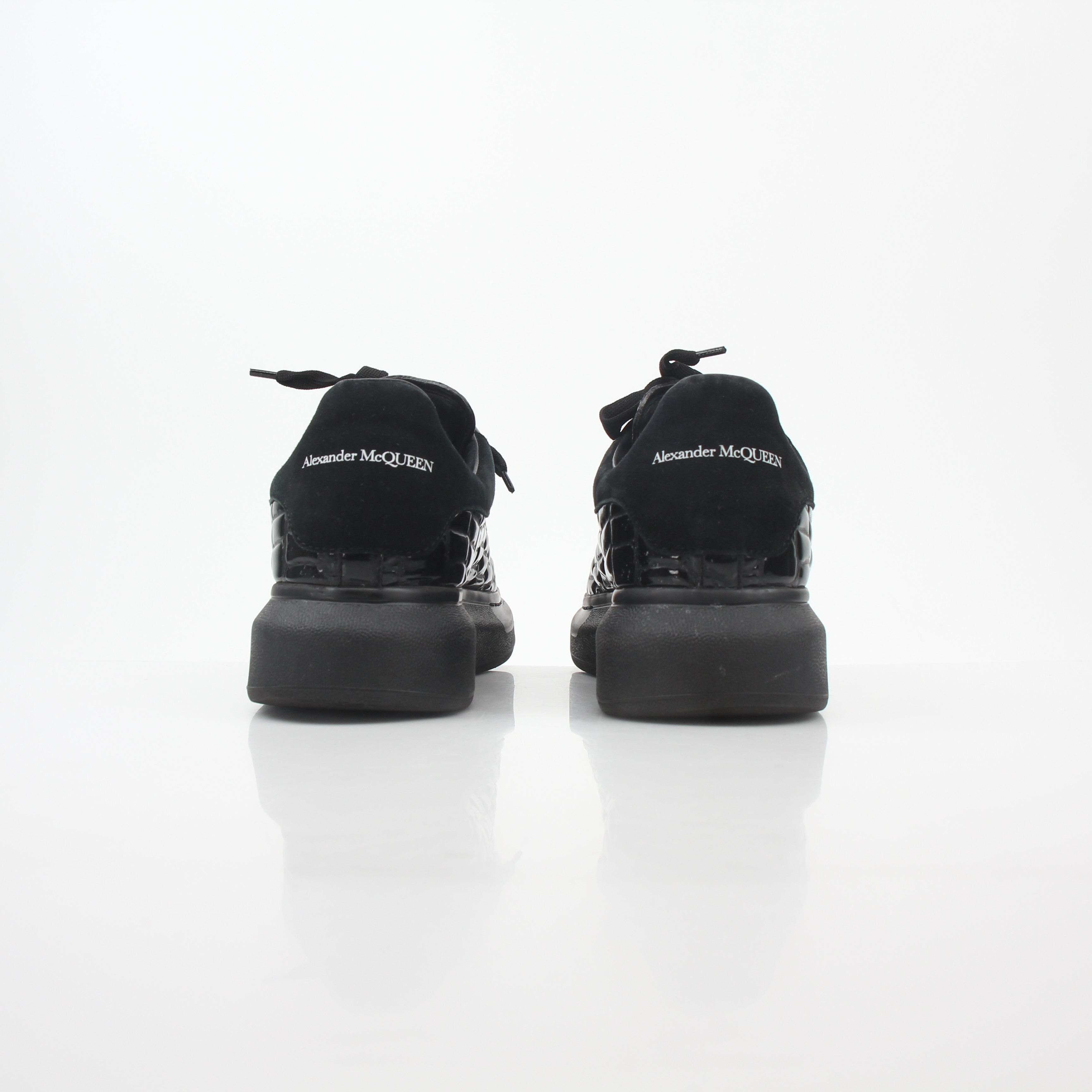 Black croc-embossed Alexander McQueen oversized sneakers with chunky soles, stylishly displayed on a white background.