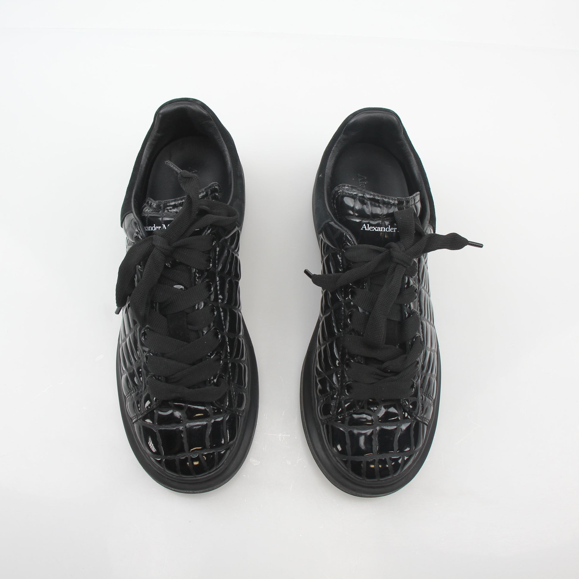 Black croc-embossed oversized Alexander McQueen sneakers with chunky design and white soles, displayed in a fashion shot.