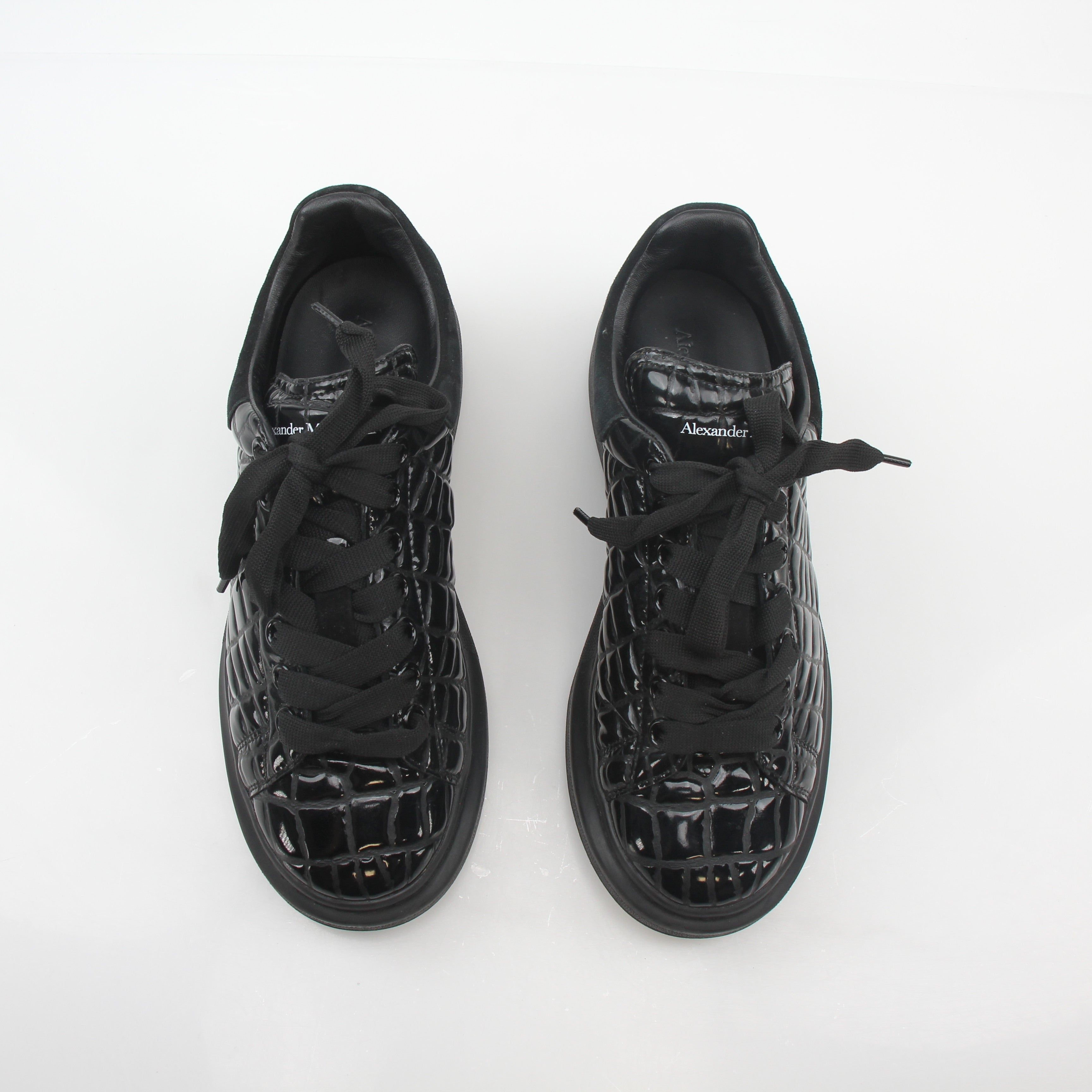 Black croc-embossed oversized Alexander McQueen sneakers with chunky design and white soles, displayed in a fashion shot.