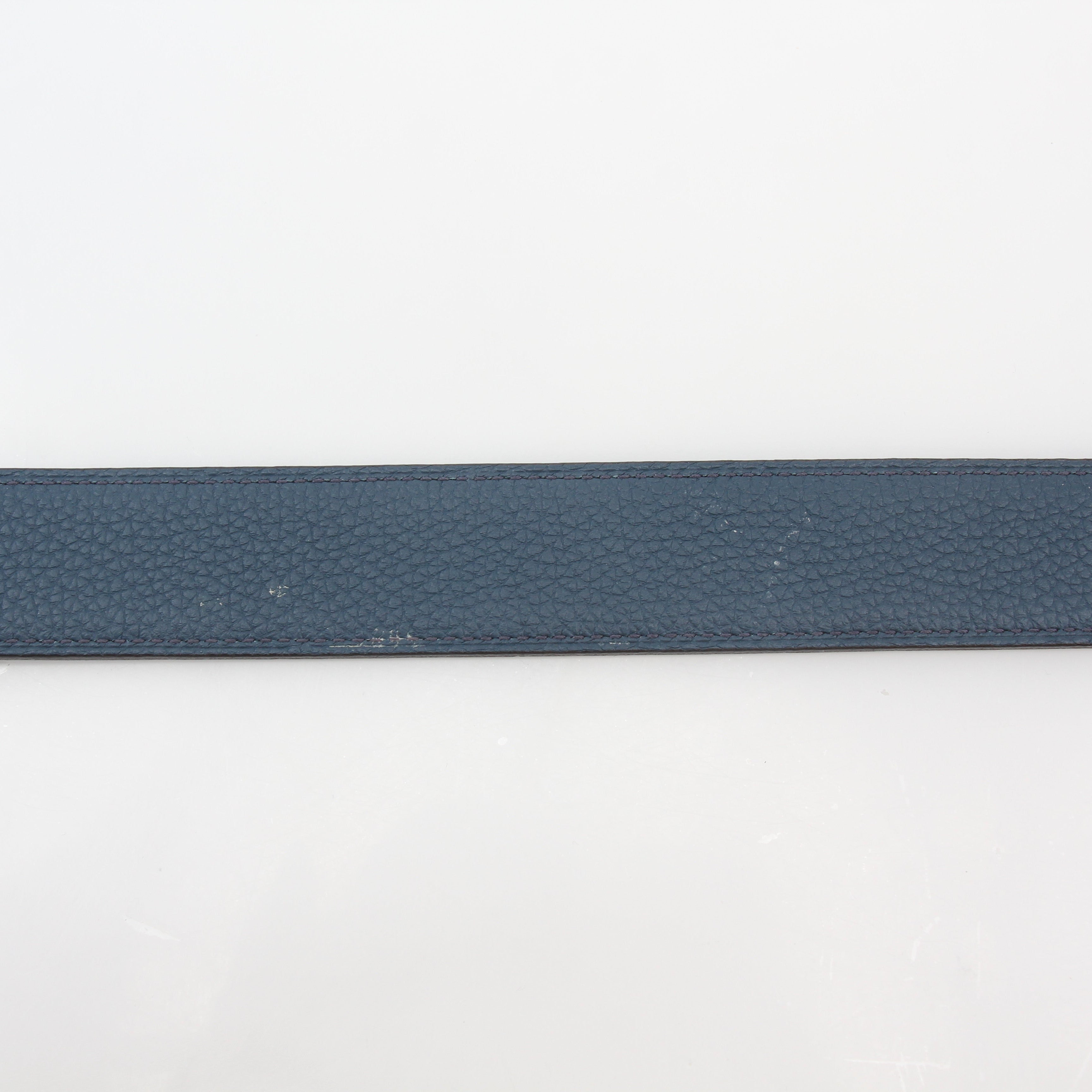 Hermès black and blue reversible belt kit with H logo, displayed with belt buckle and accessories on a neutral background.