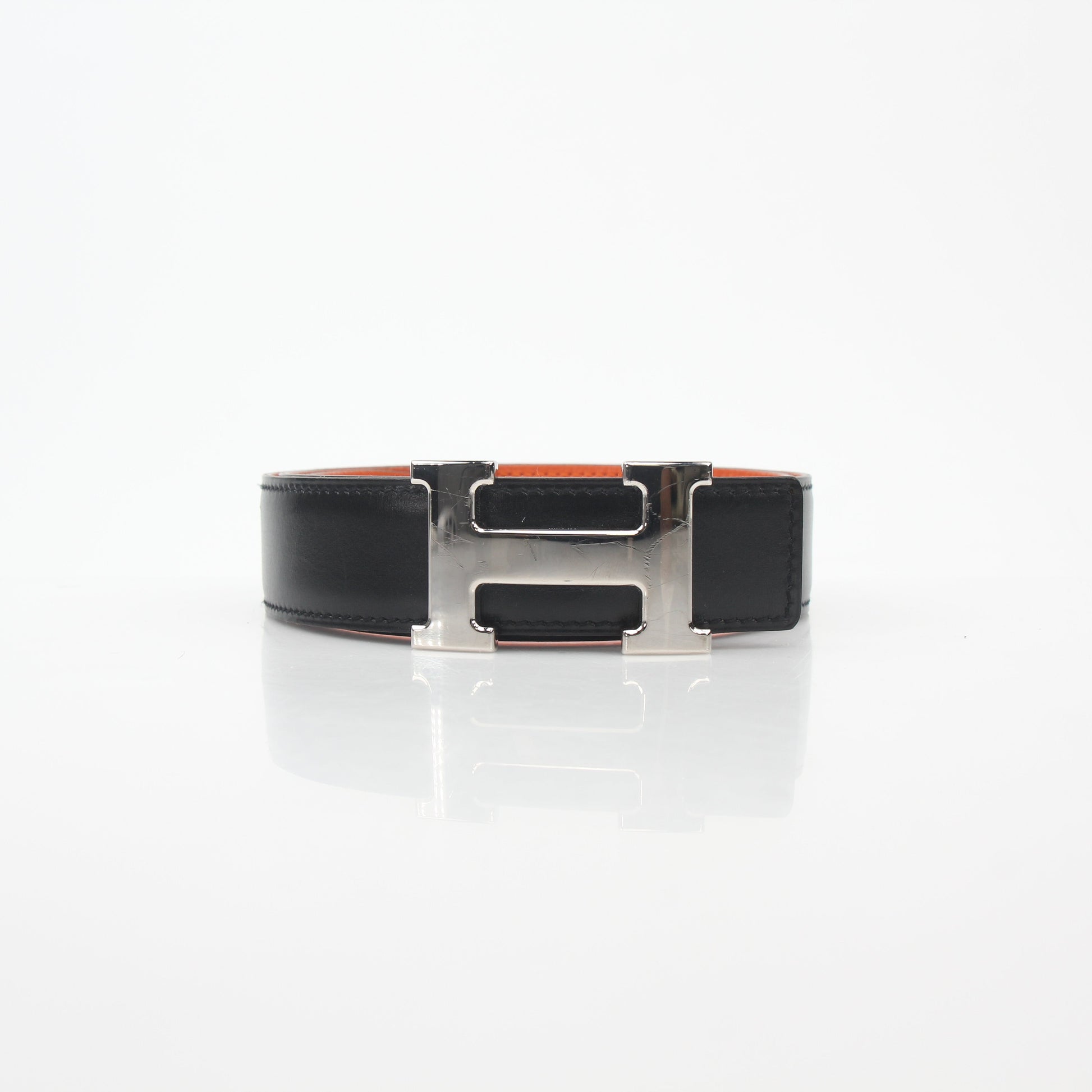 Hermès black and orange reversible belt kit with H buckle, featuring adjustable leather straps and gold-tone hardware.