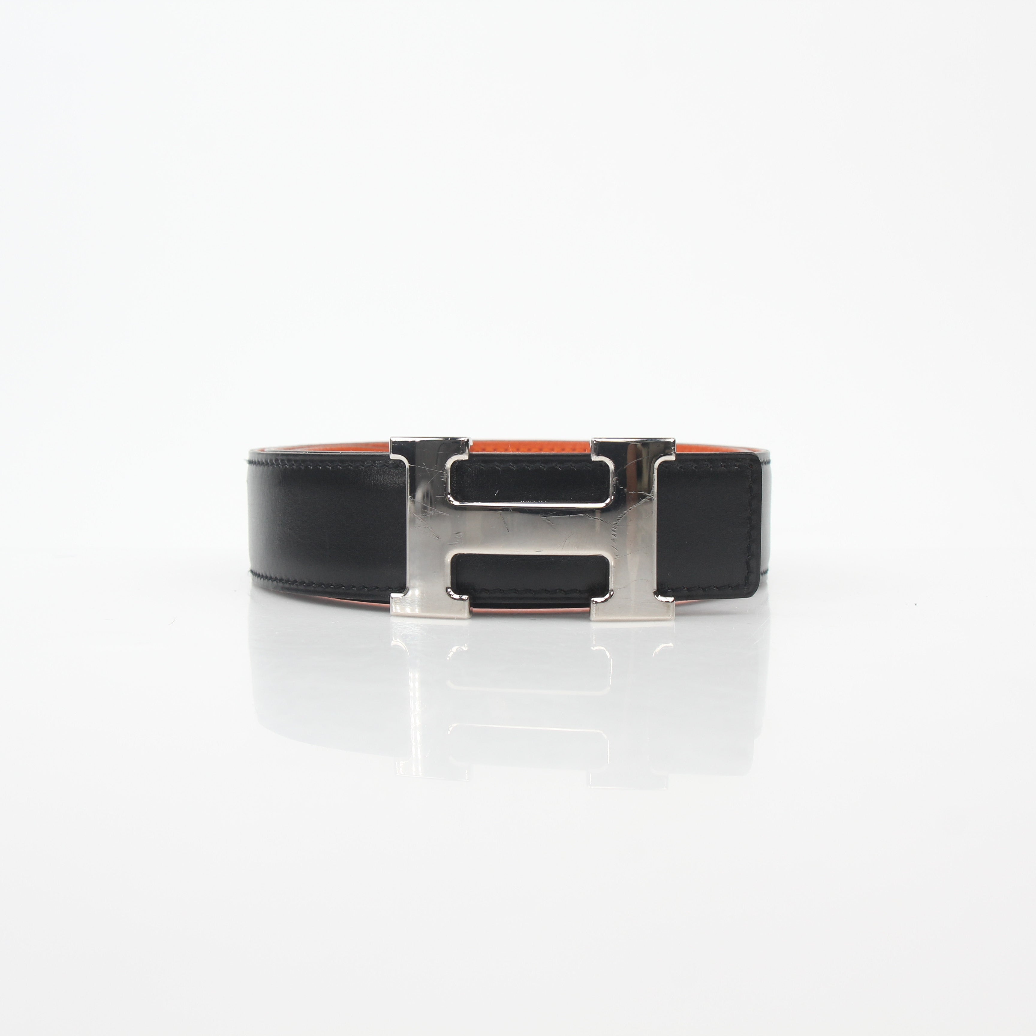 Hermès black and orange reversible belt kit with H buckle, featuring adjustable leather straps and gold-tone hardware.