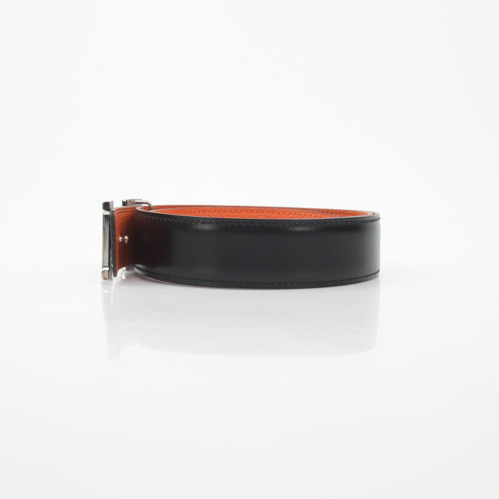 Hermès black and orange reversible belt kit with H buckle, featuring textured leather and versatile accessory design.