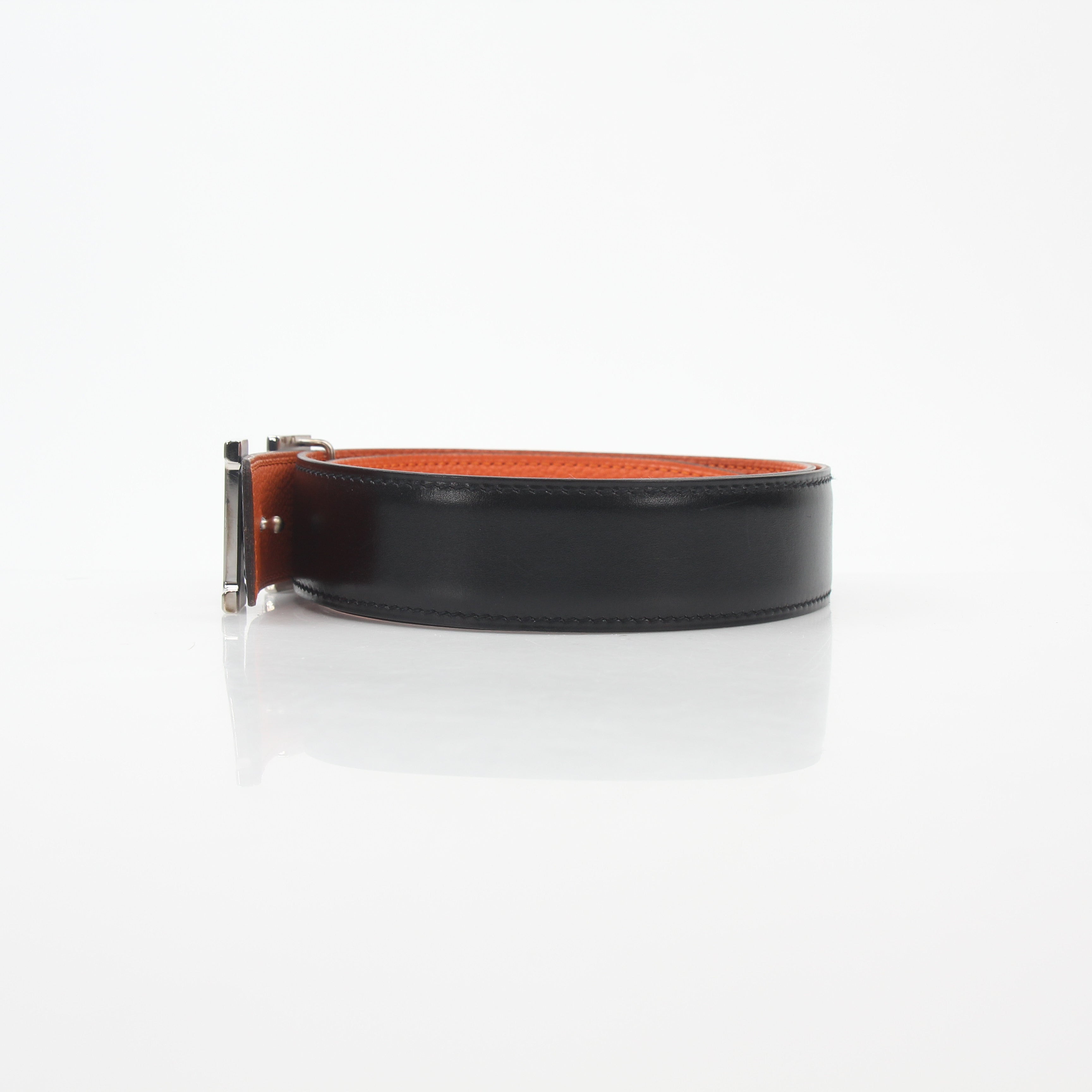 Hermès black and orange reversible belt kit with H buckle, featuring textured leather and versatile accessory design.