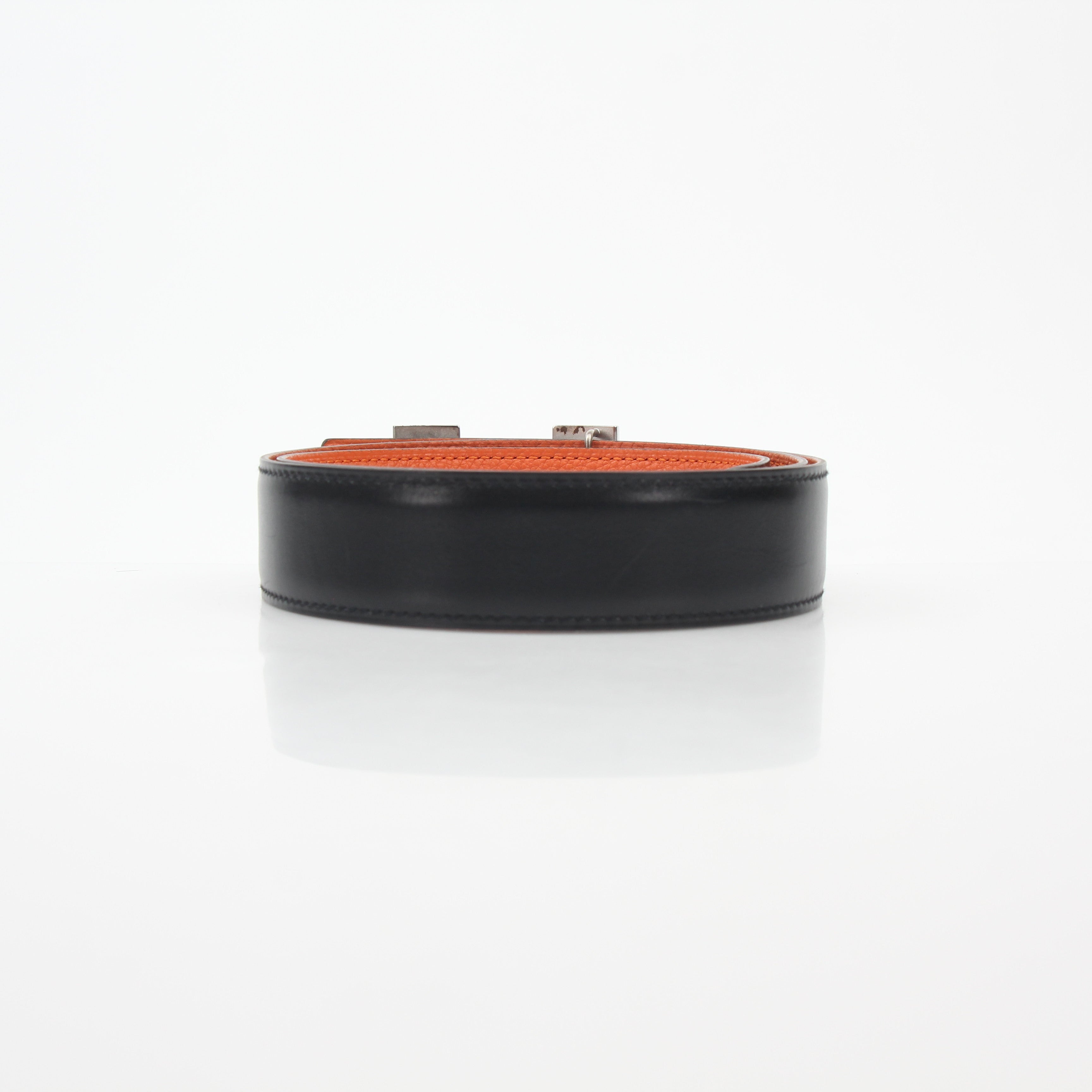 Hermès black and orange reversible belt kit with H buckle, accessories by Gold & Beyond, showing the belt laid flat with reversible design.