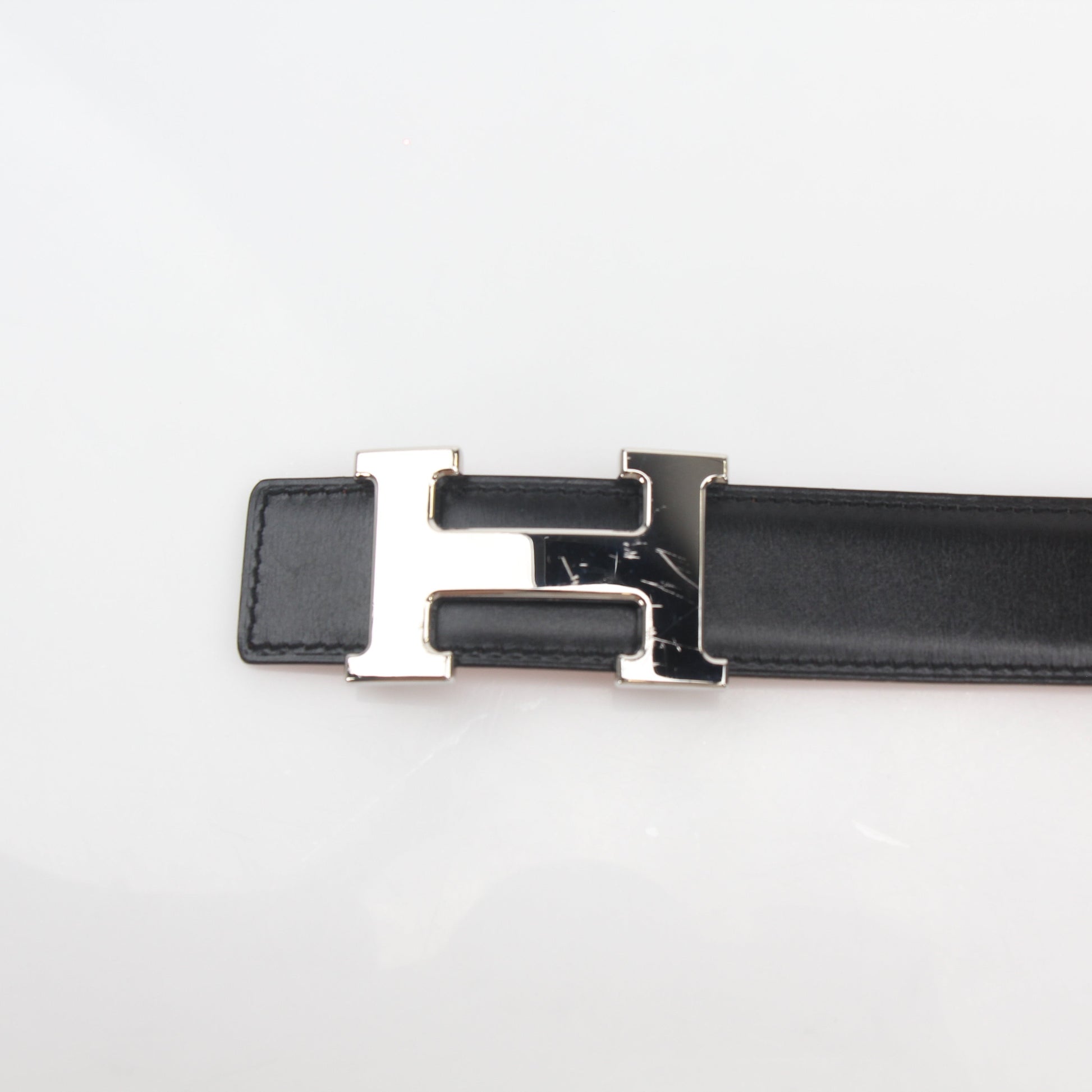 Hermès black and orange H reversible belt kit with gold tone hardware, displayed with accessories on a neutral background.