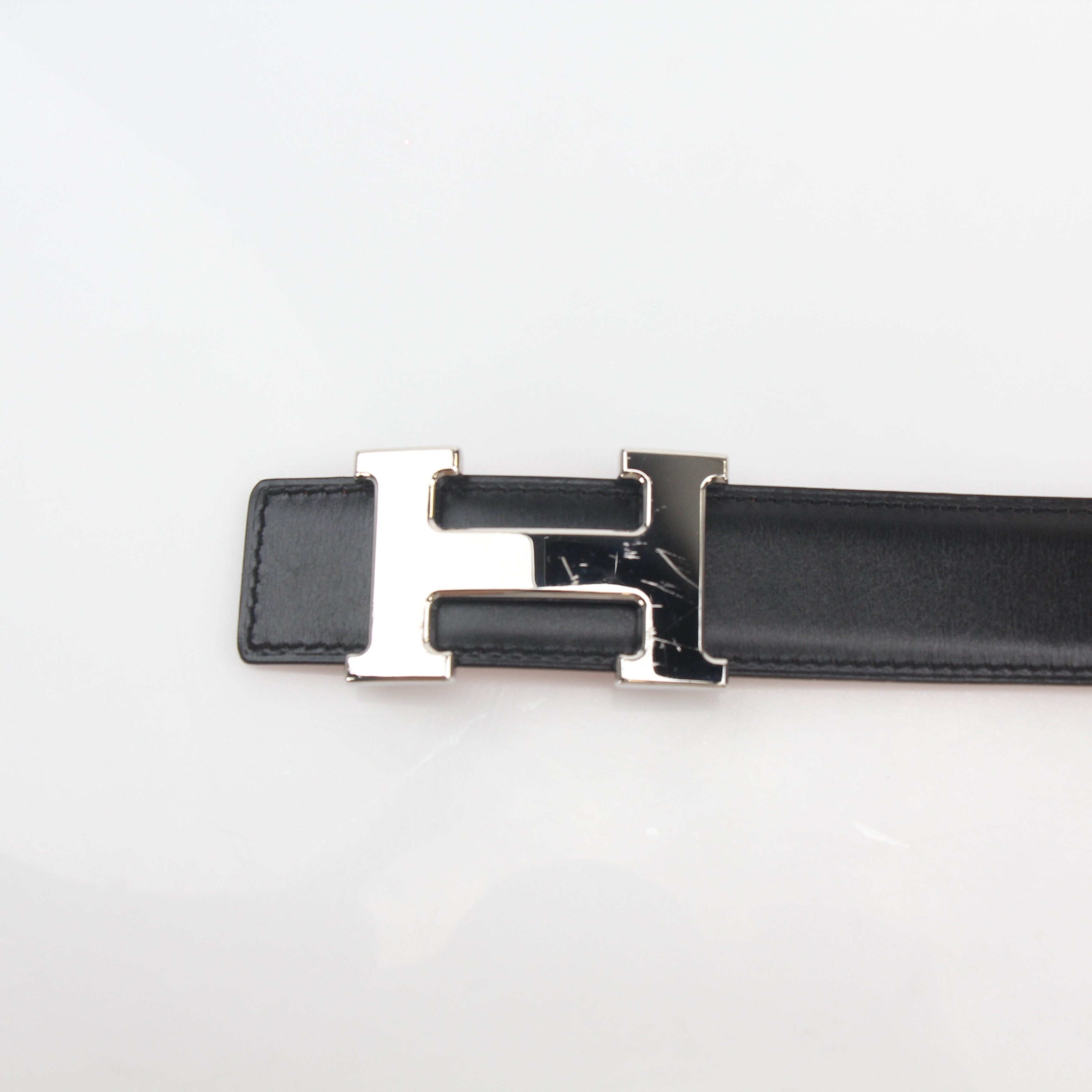Hermès black and orange H reversible belt kit with gold tone hardware, displayed with accessories on a neutral background.