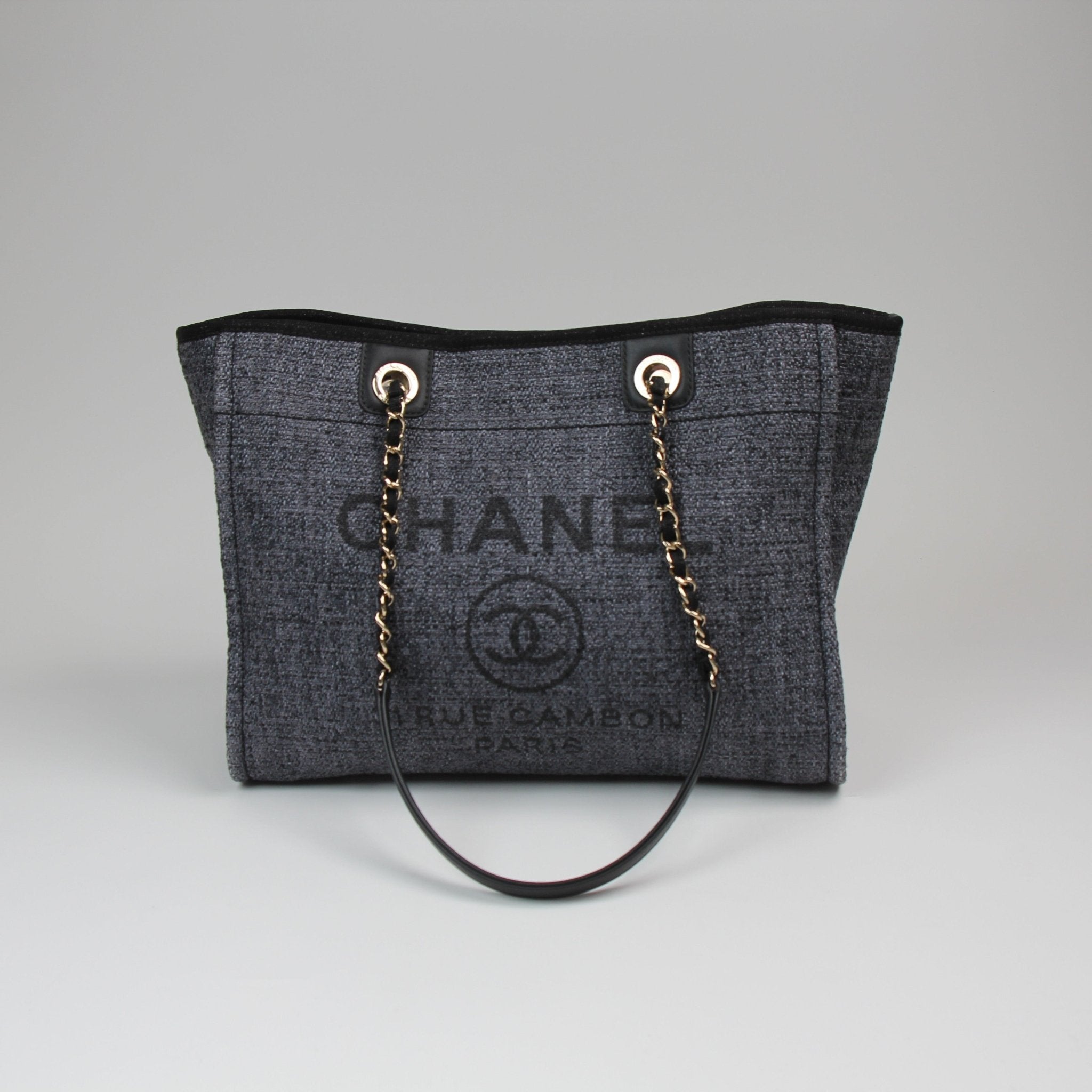 Chanel Deauville Tweed Tote bag with leather handles and gold accents, featuring a classic beige and black tweed pattern.