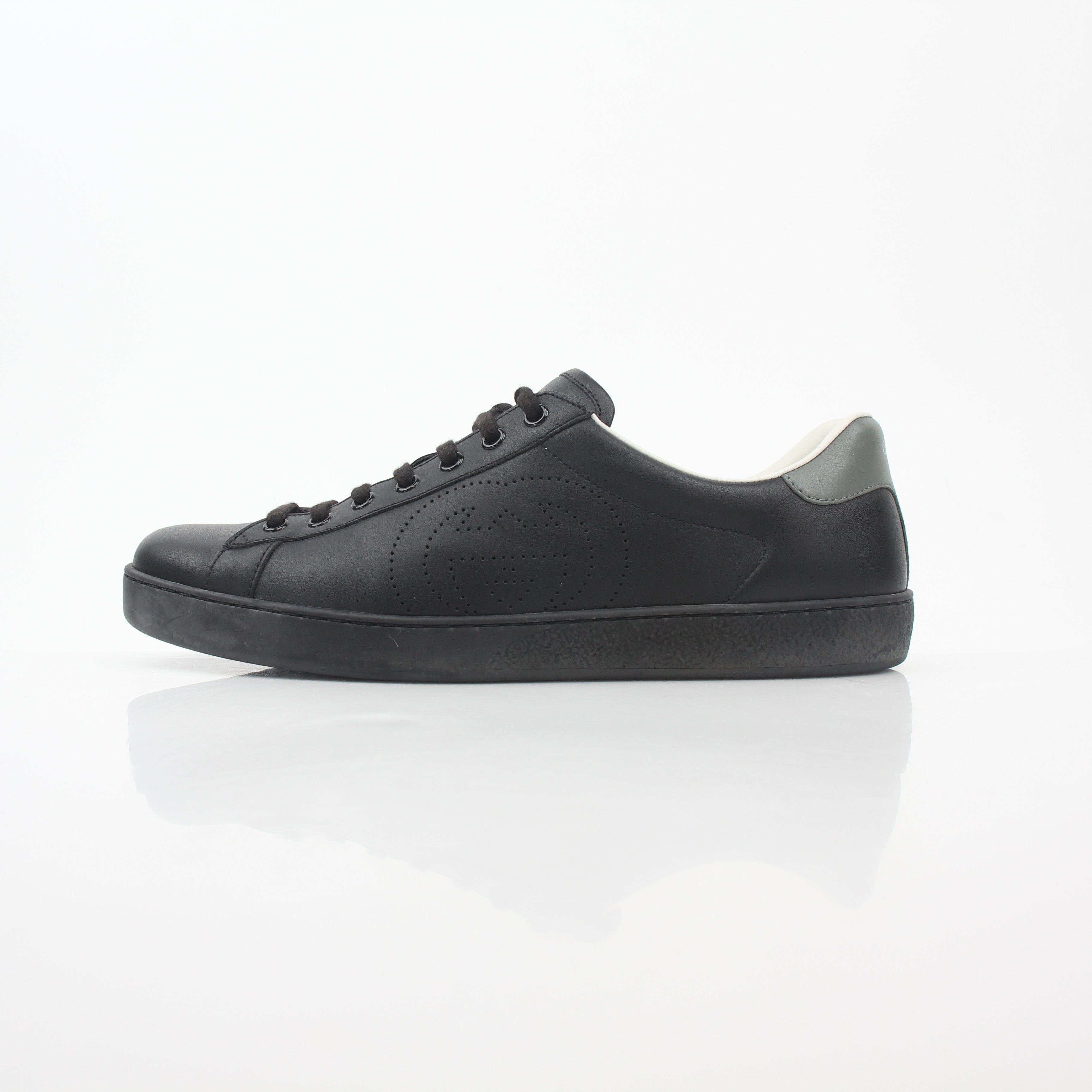 Black leather Gucci Brooklyn low-top sneakers with white soles and gold accents, displayed on a neutral background.