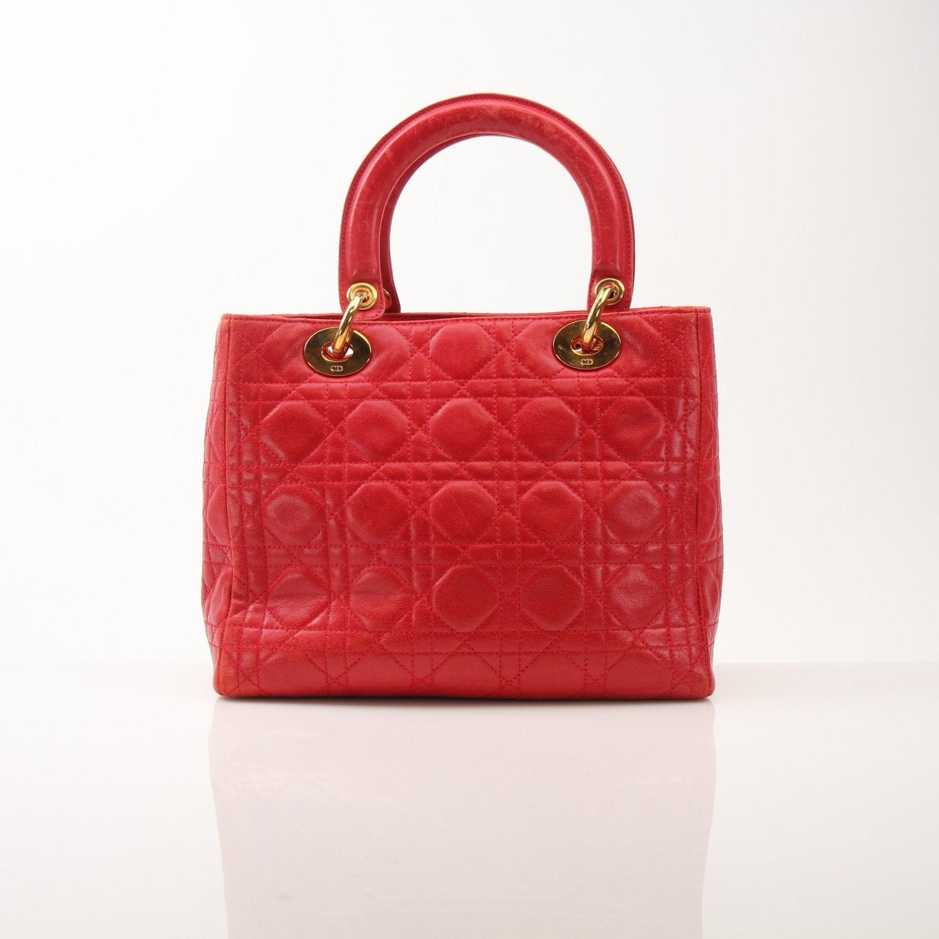 Red Christian Dior Lady Dior handbag with top handle and gold accents, featuring elegant design, displayed on a neutral background.