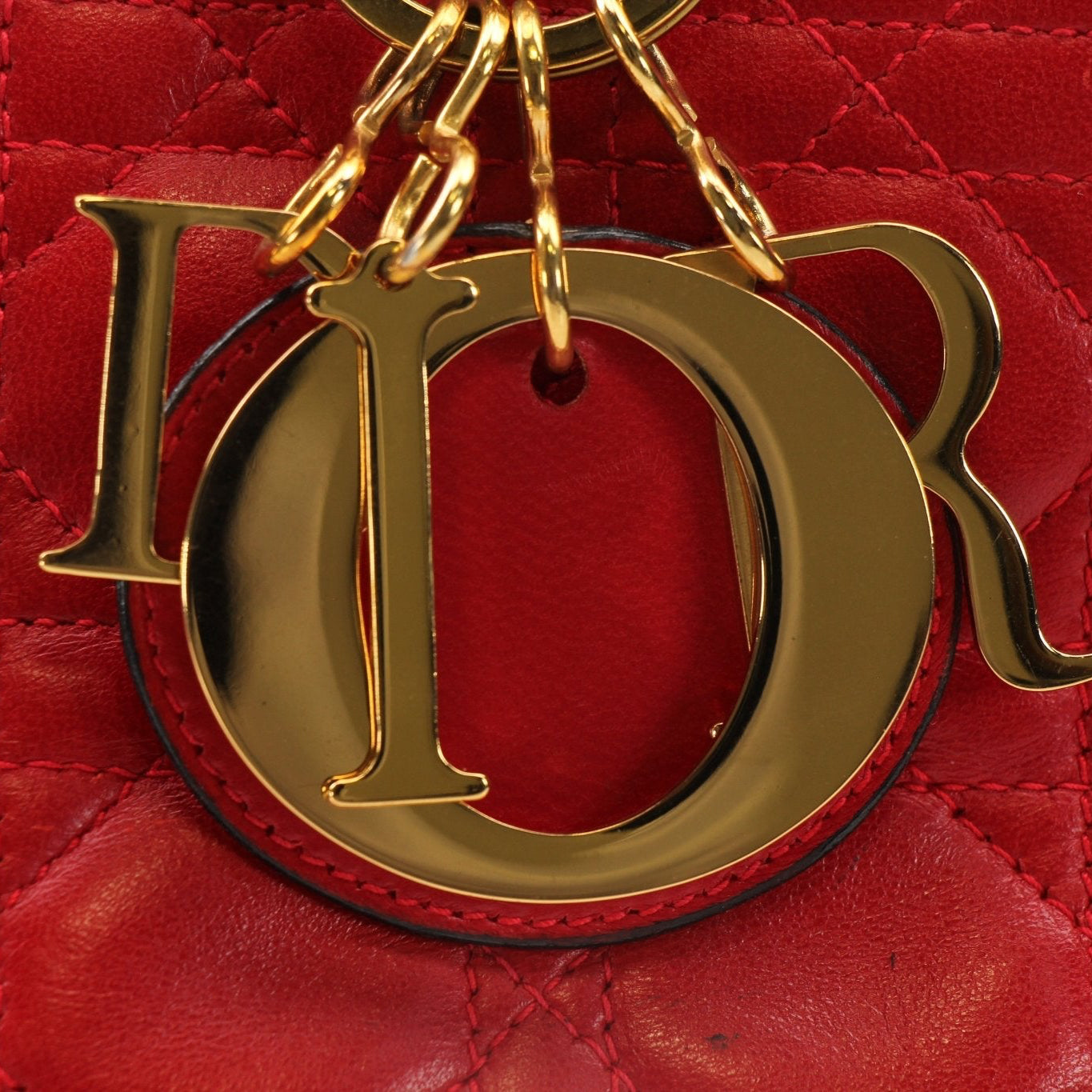 Red Christian Dior Lady Dior handbag with top handle and gold accents, stylishly displayed against a neutral background.