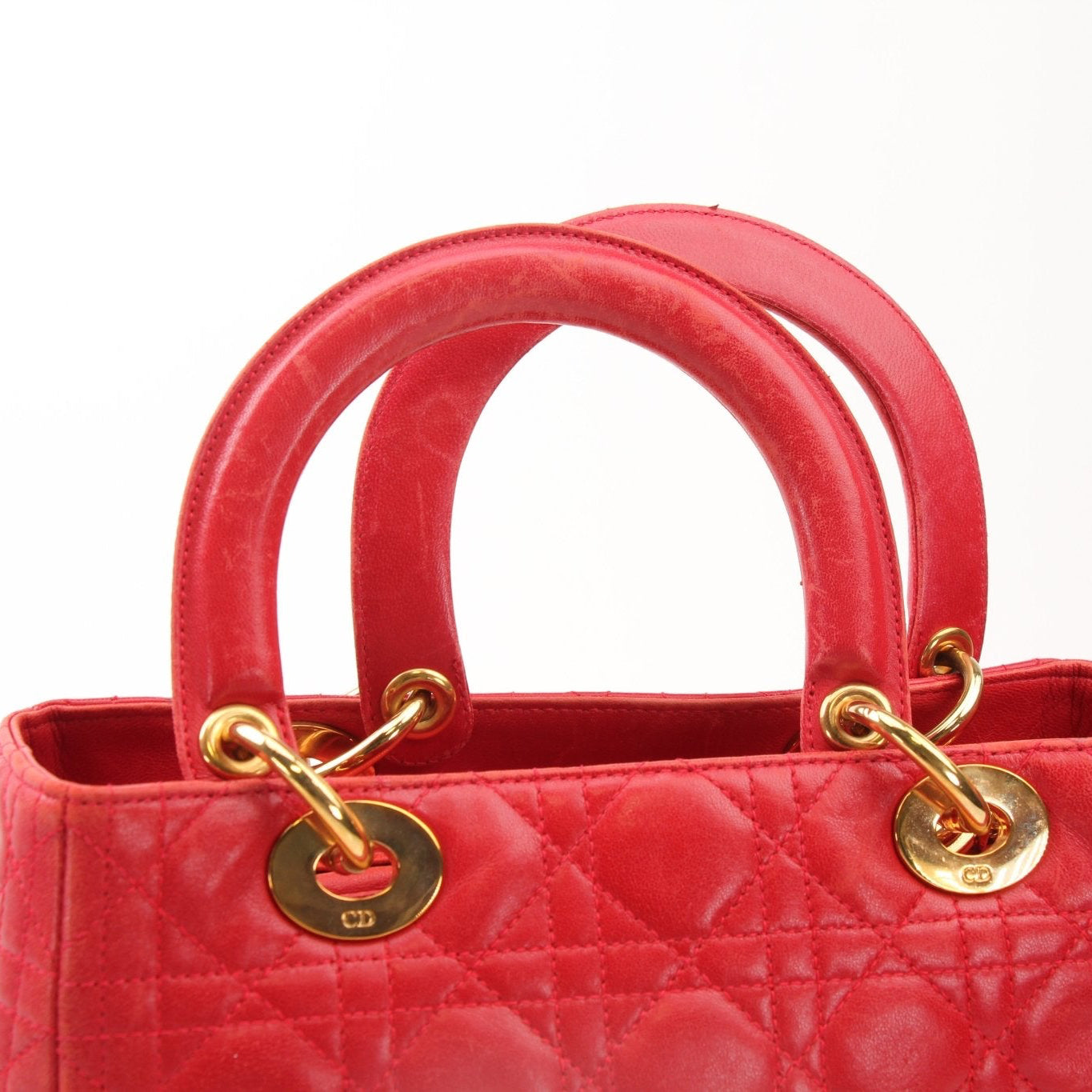 Red Christian Dior Lady Dior handbag with top handle, featuring gold accents and elegant design, shown in a close-up image.