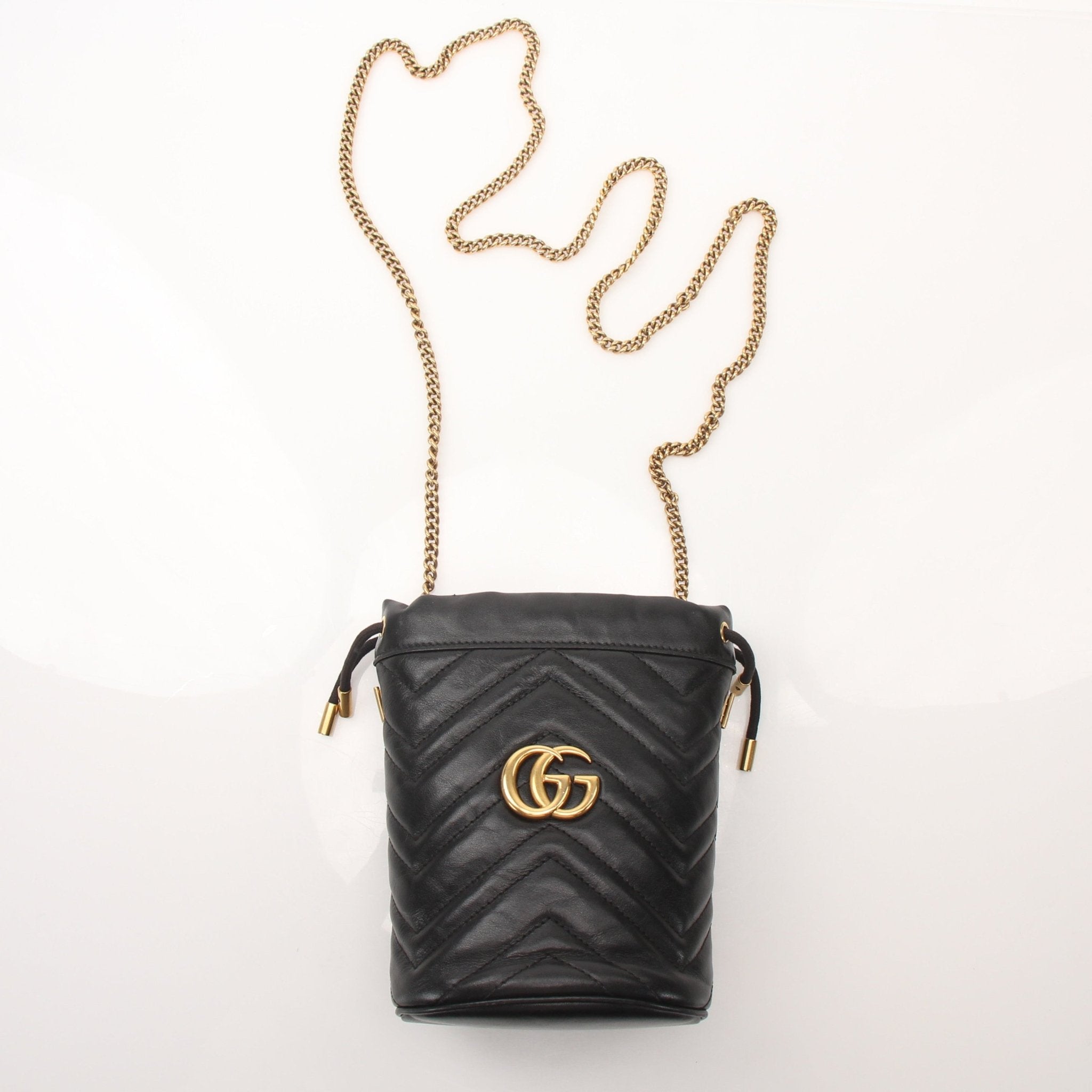 Gucci GG Marmont small bucket handbag in black leather with gold hardware and adjustable strap, displayed on a white background.