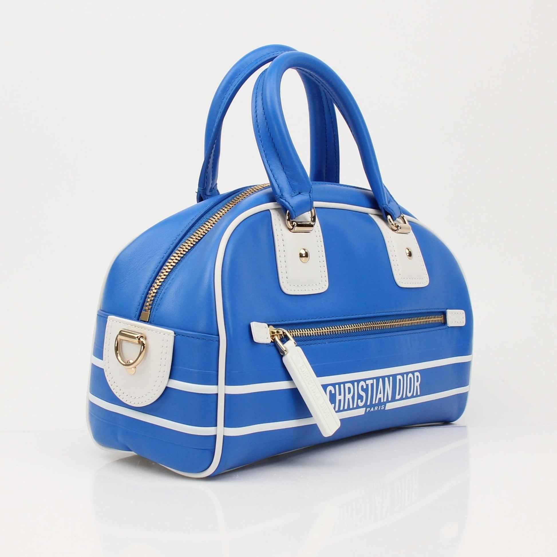 Christian Dior blue bowling handbag with gold accents, stylish and spacious designer hand-held bag displayed against a neutral background.