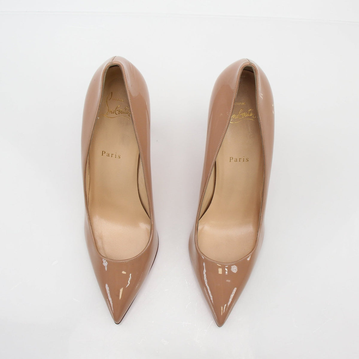 Christian Louboutin Nude Pigalle 100 patent leather pumps with pointed toes and sleek heel, showcased on a white background.