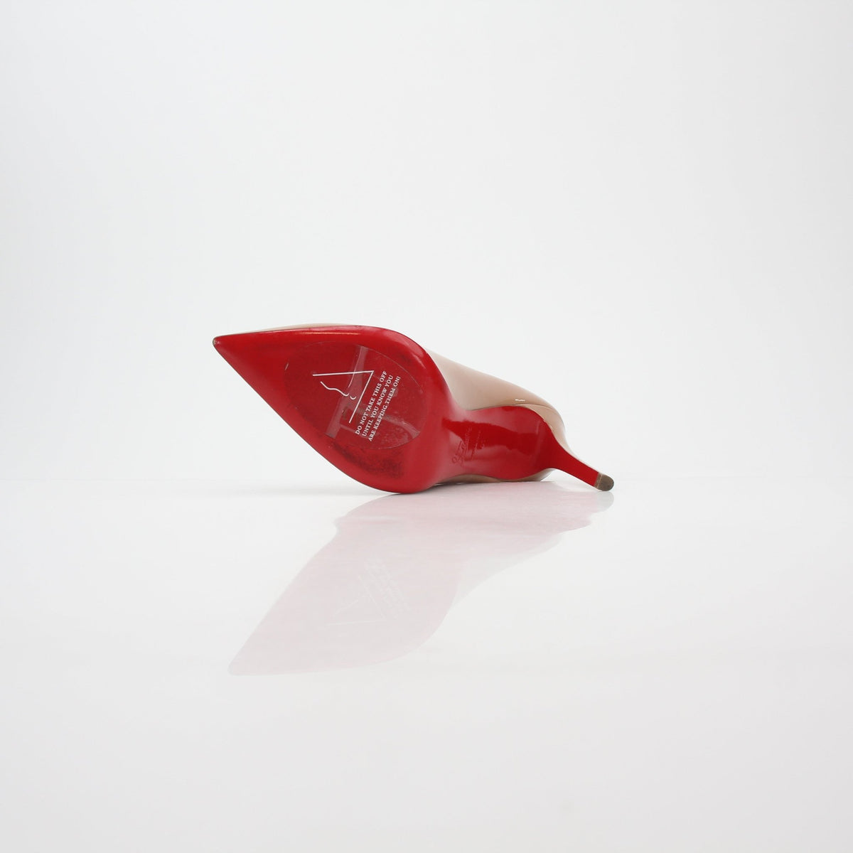 Christian Louboutin Nude Pigalle 100 patent leather heels with pointed toes and signature red soles, displayed on a neutral surface.