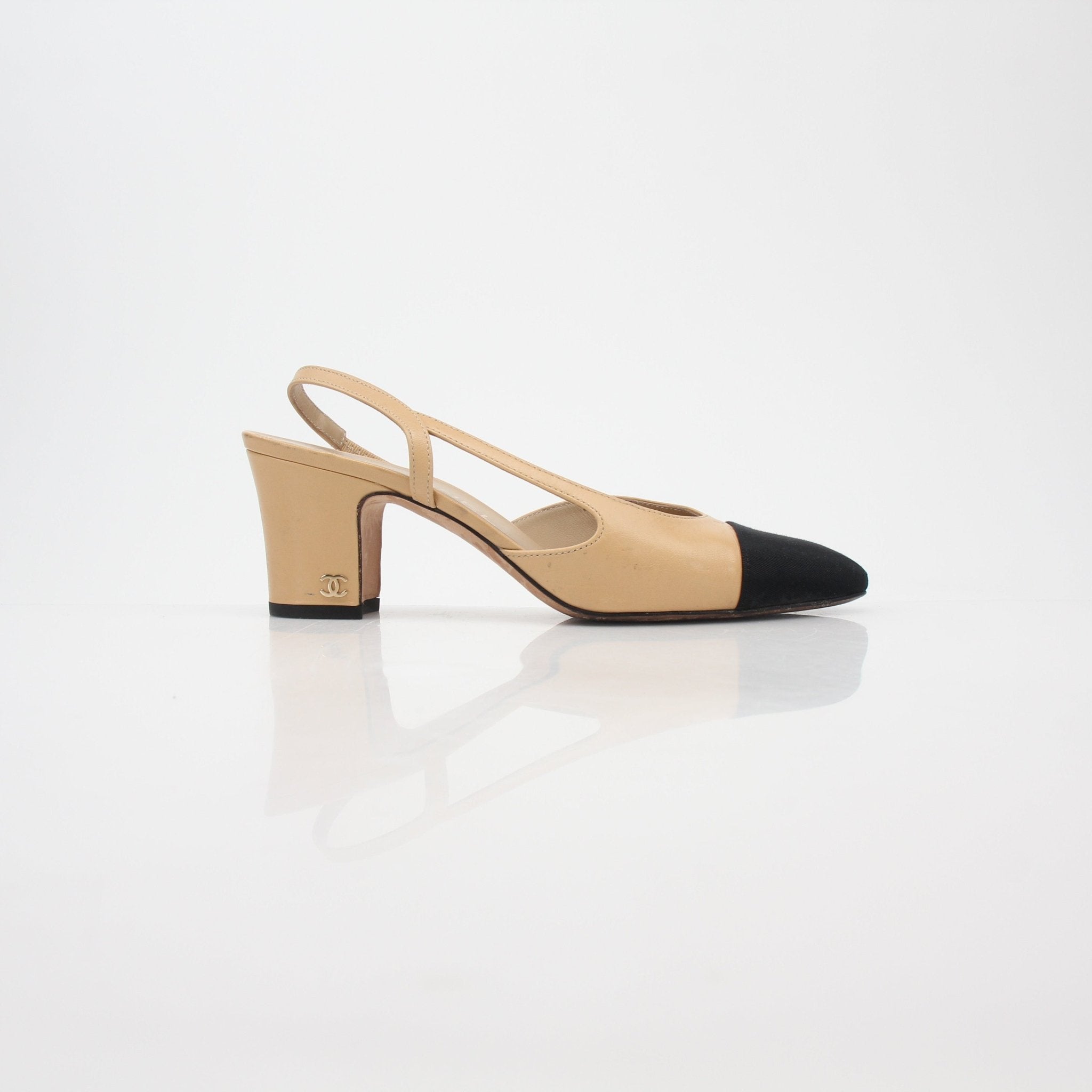 Gold & Beyond beige and black Chanel cap-toe slingback pumps with mid-height heels on a neutral background.