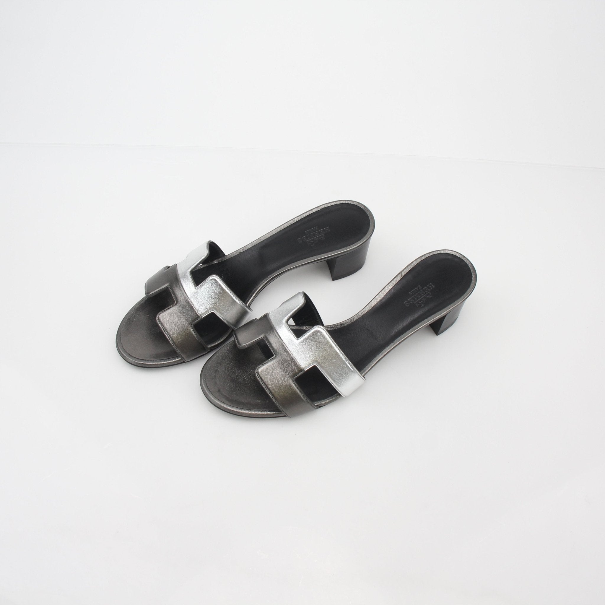 Hermès Metallic Silver Oasis sandals by Gold & Beyond, featuring sleek metallic straps and stylish design on a pair of shoes.