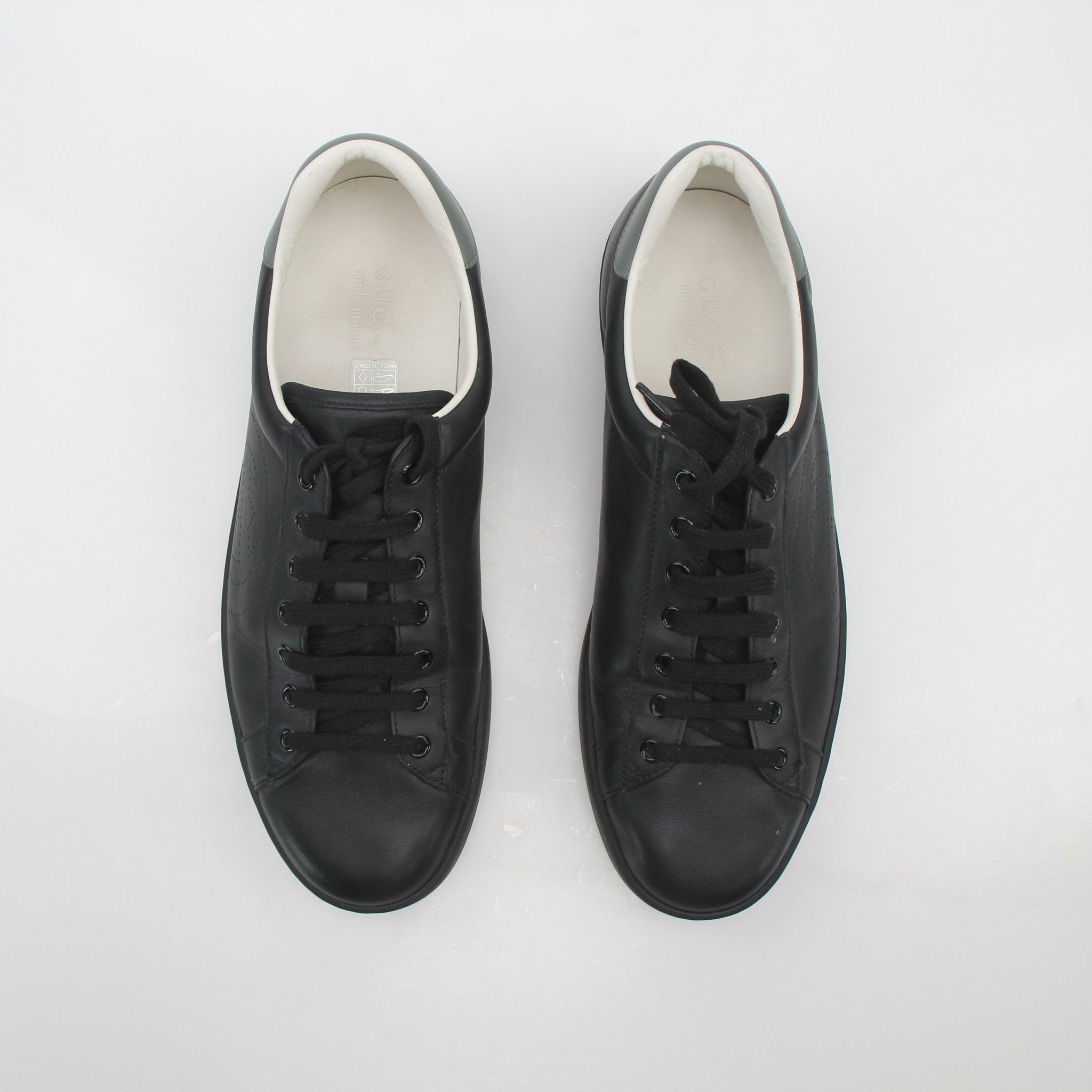 Black Gucci Ace perforated leather sneakers with interlocking G logo, displayed on a plain background.