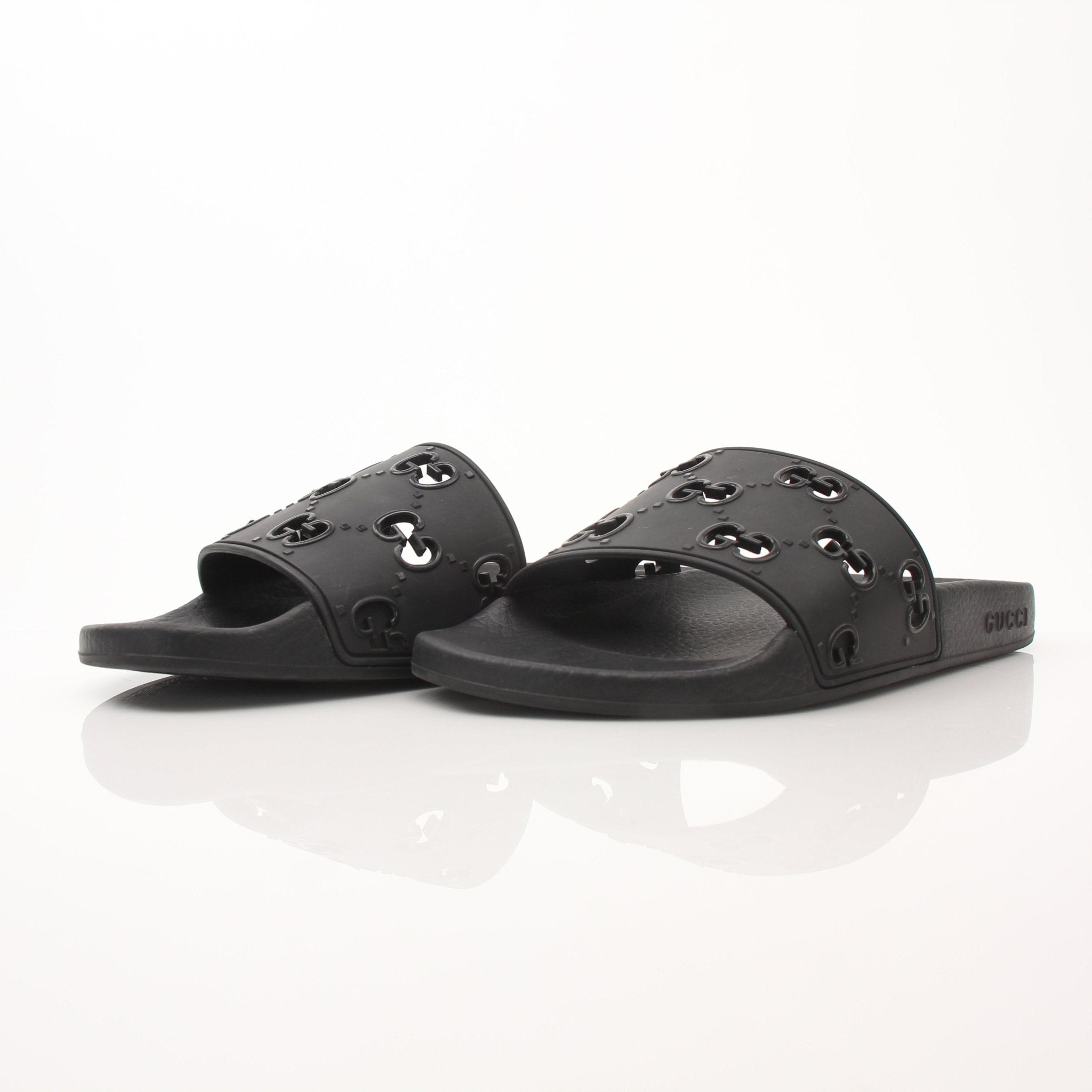 Gold & Beyond Gucci Pursuit Slides shoes featuring black straps and a sleek design, displayed on a plain background.