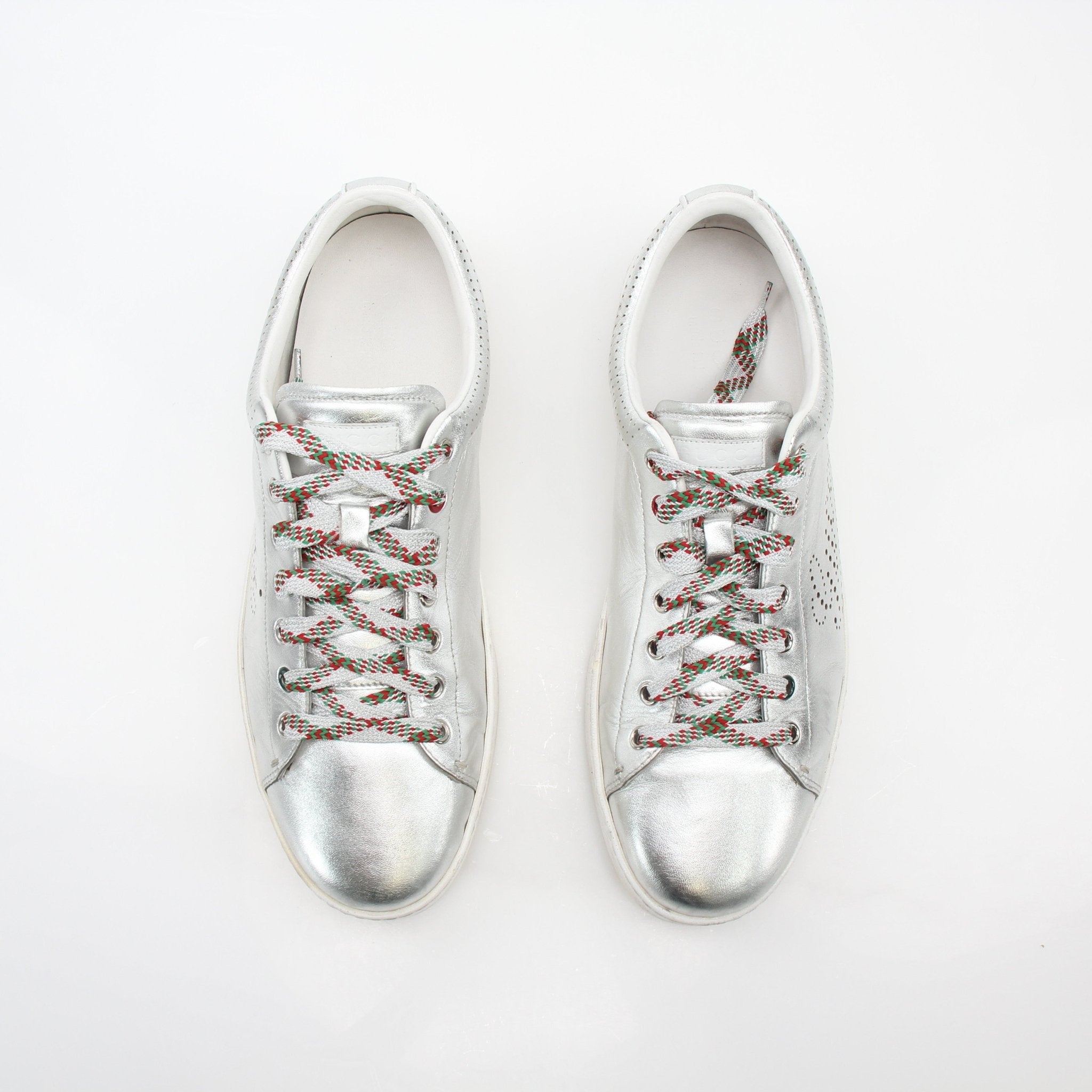 Silver metallic Gucci Ace perforated logo sneakers with white rubber soles and branded detailing, styled on a plain background.