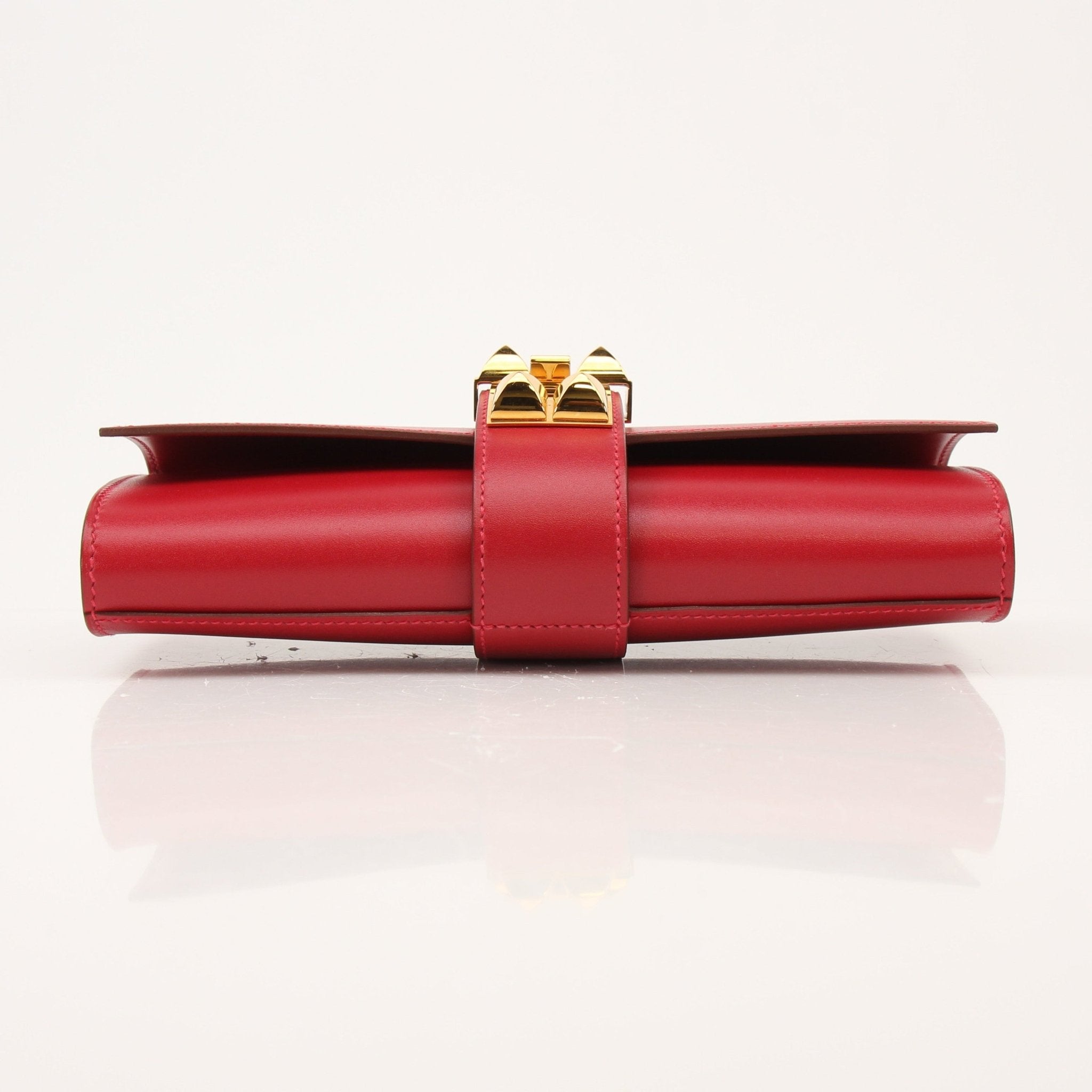 Hermès Médor 23 red clutch handbag with gold hardware, featuring a sleek design and textured leather surface.