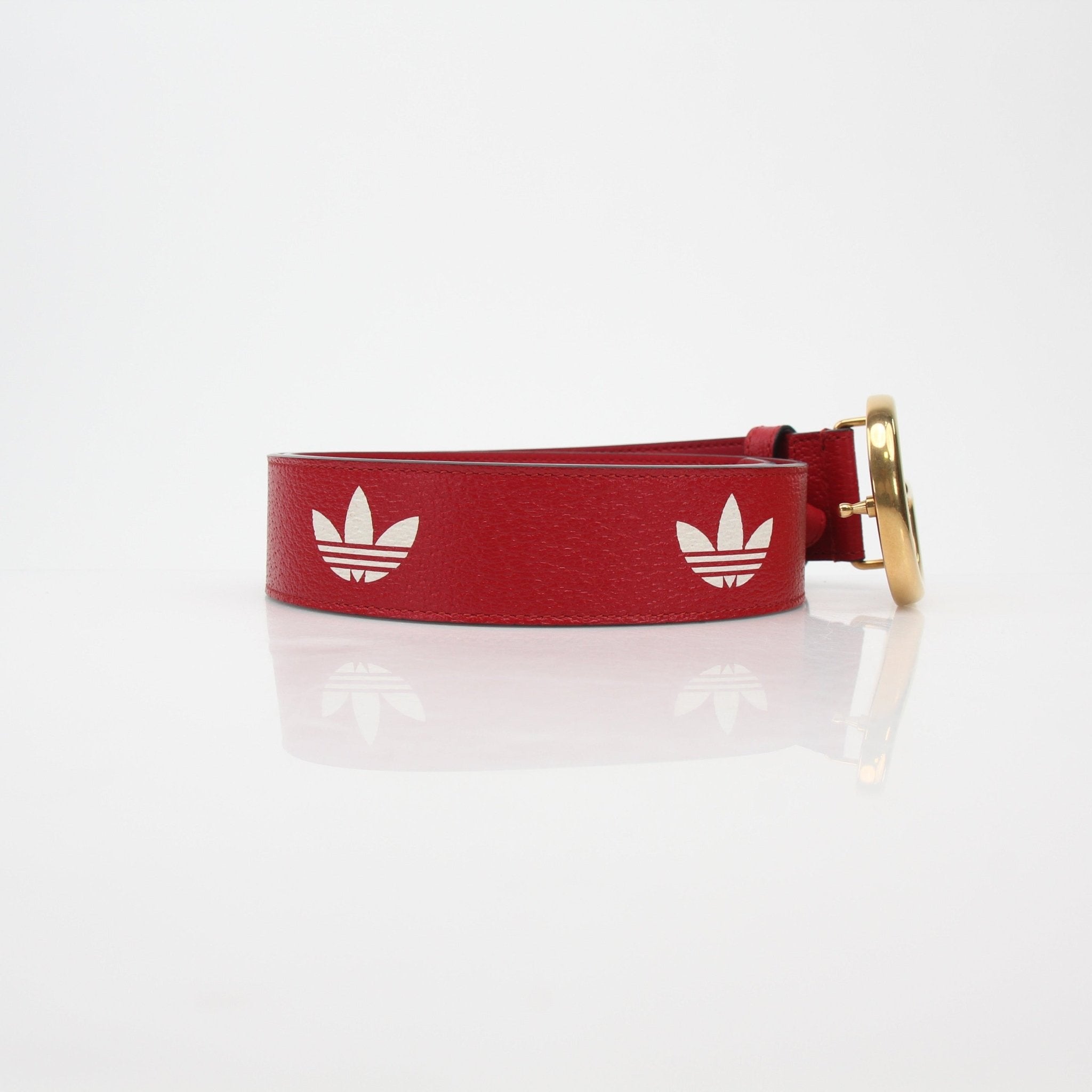 Red leather Gucci GG Marmont belt with gold hardware from Adidas x Gucci accessories collection, displayed on a neutral background.