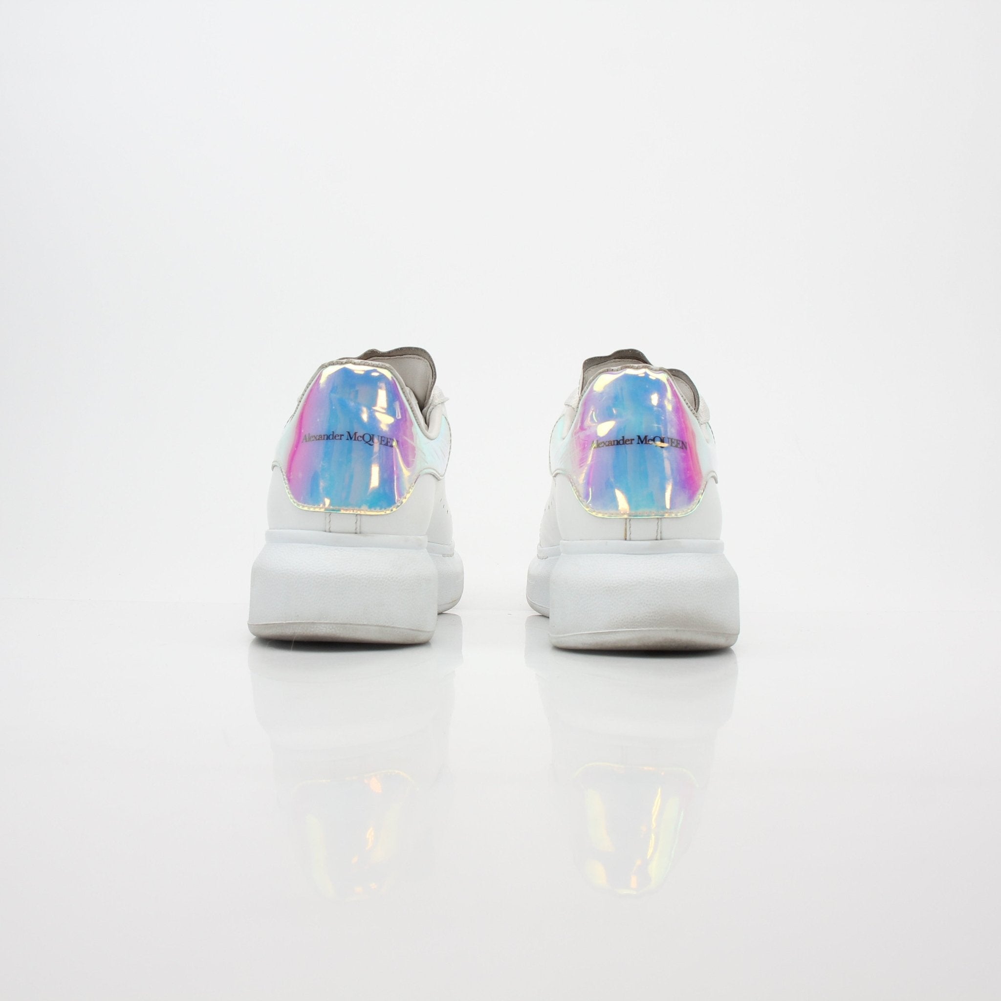 Alexander McQueen white oversized iridescent heel sneakers with chunky soles and bold design, worn on a clean background.