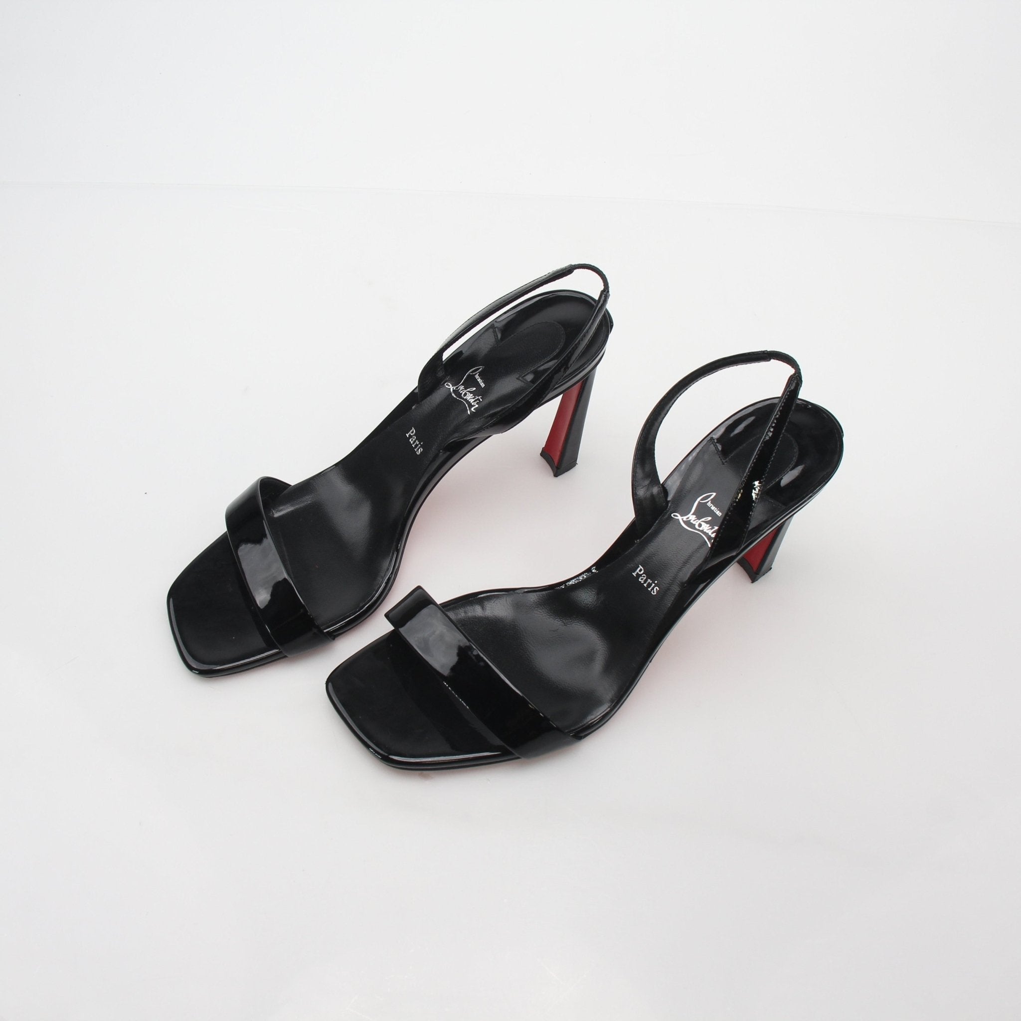 Black Christian Louboutin Condora Queen patent leather heels with ankle straps and signature red soles.
