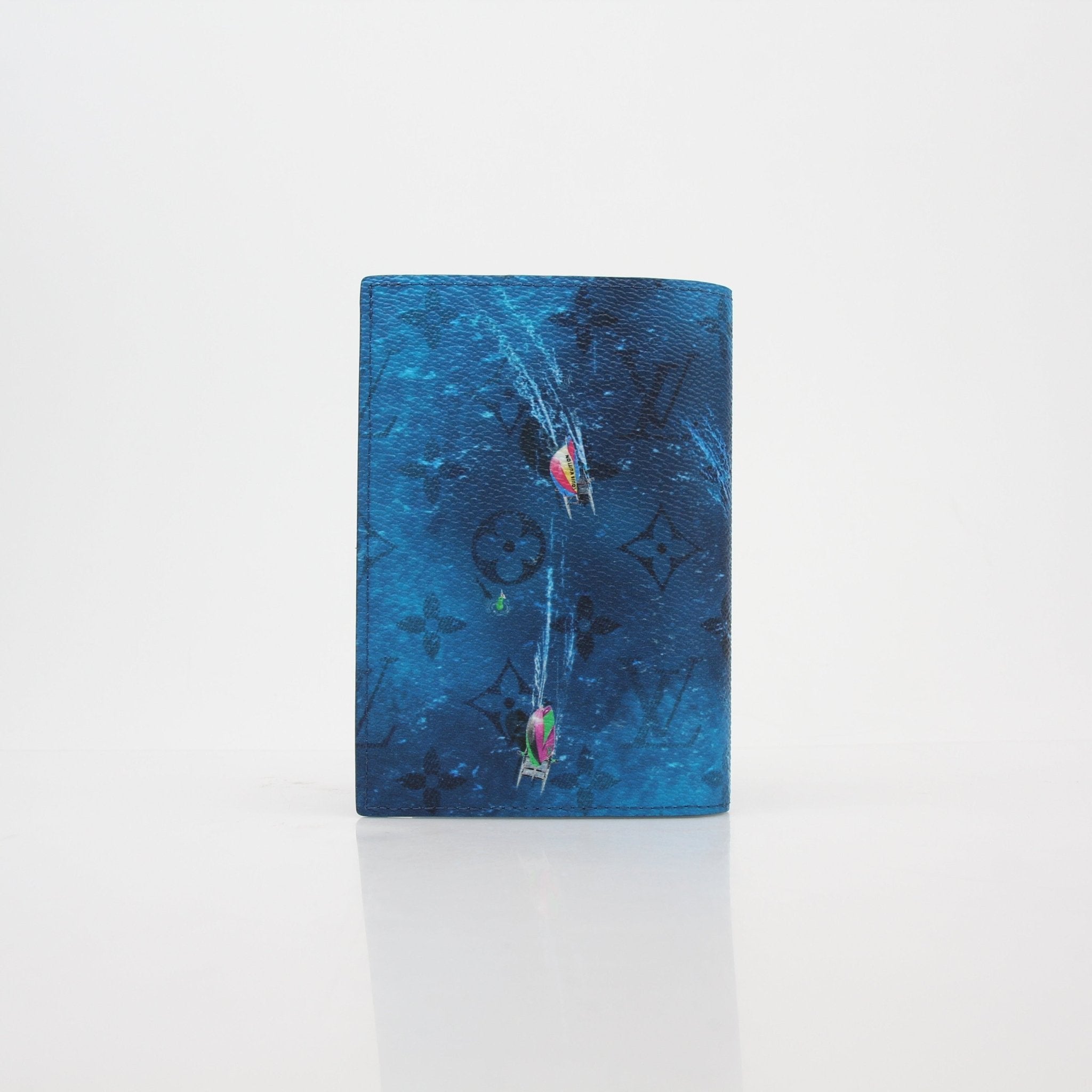 Louis Vuitton blue monogram Catamaran passport cover wallet with gold accents and branded interior, displayed on a white background.