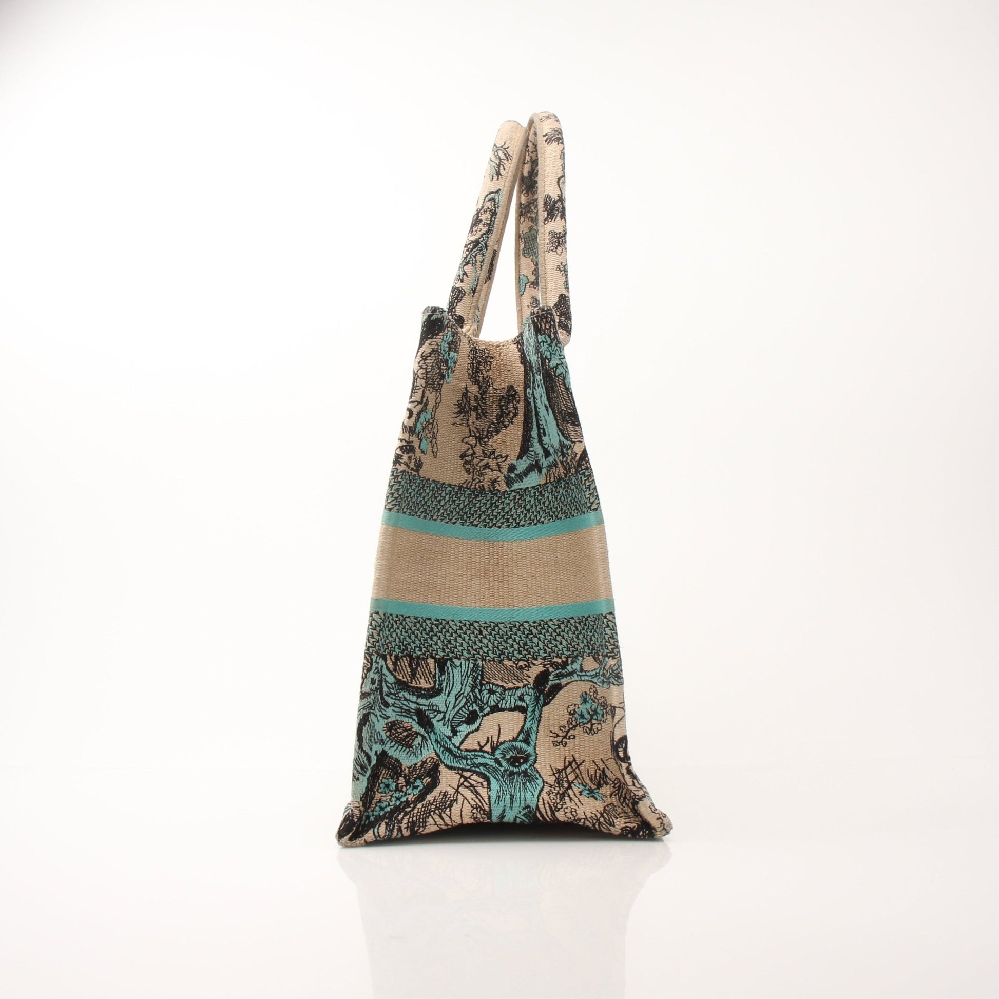 Christian Dior Book Tote handbag with floral pattern and leather handles, stylishly displayed with a background of greenery.