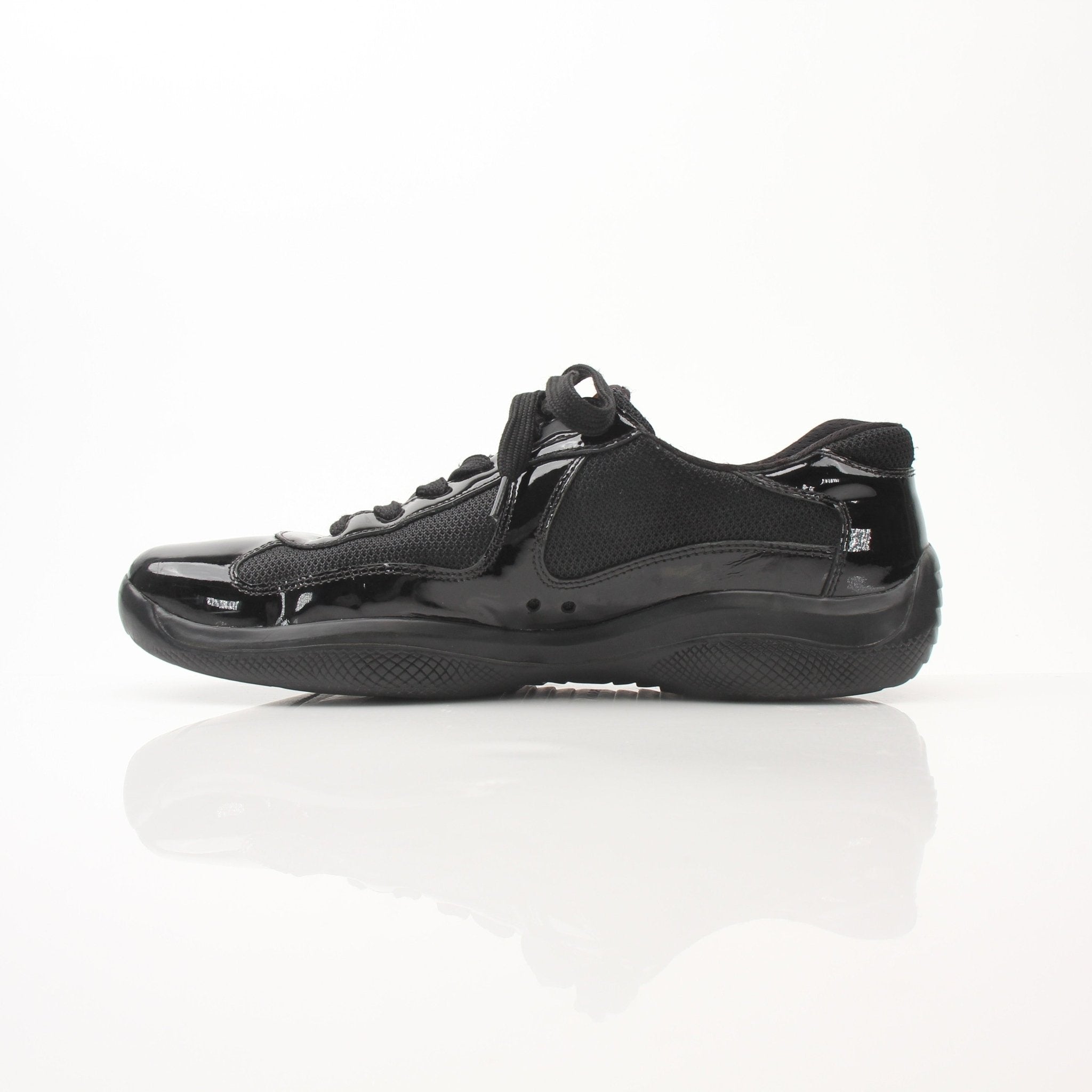 Prada men's black patent leather sneakers with gold accents, featuring a sleek design and sporty style.