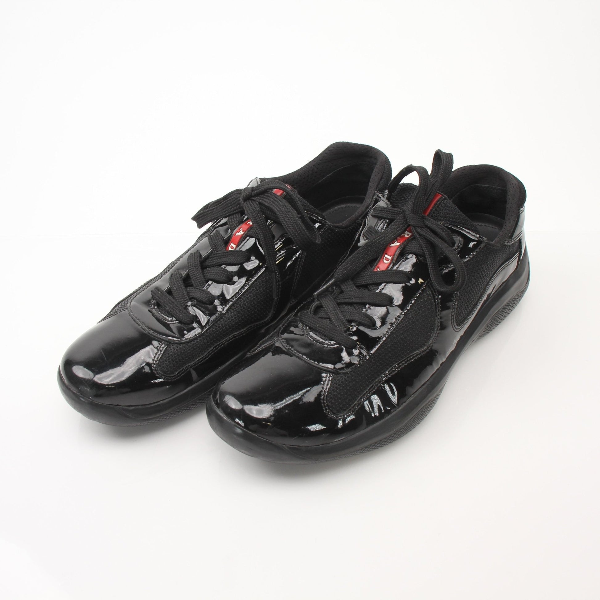 Prada men's black patent leather sneakers with sleek design, photographed from the side showing the stylish shoe details.