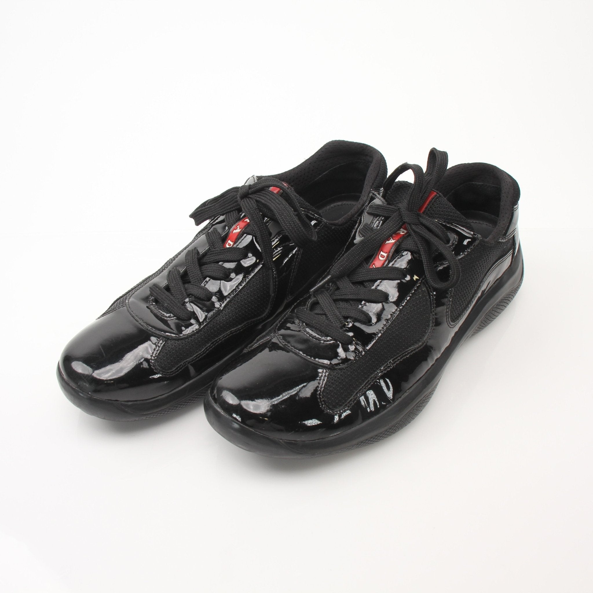 Prada men's black patent leather sneakers with sleek design, photographed from the side showing the stylish shoe details.