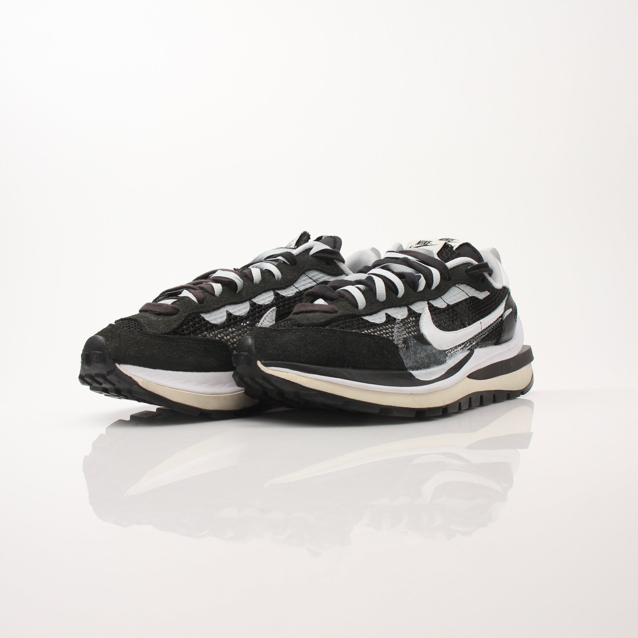 Nike x Sacai men's VaporWaffle sneakers in black and white with layered design and chunky sole, displayed on a neutral background.