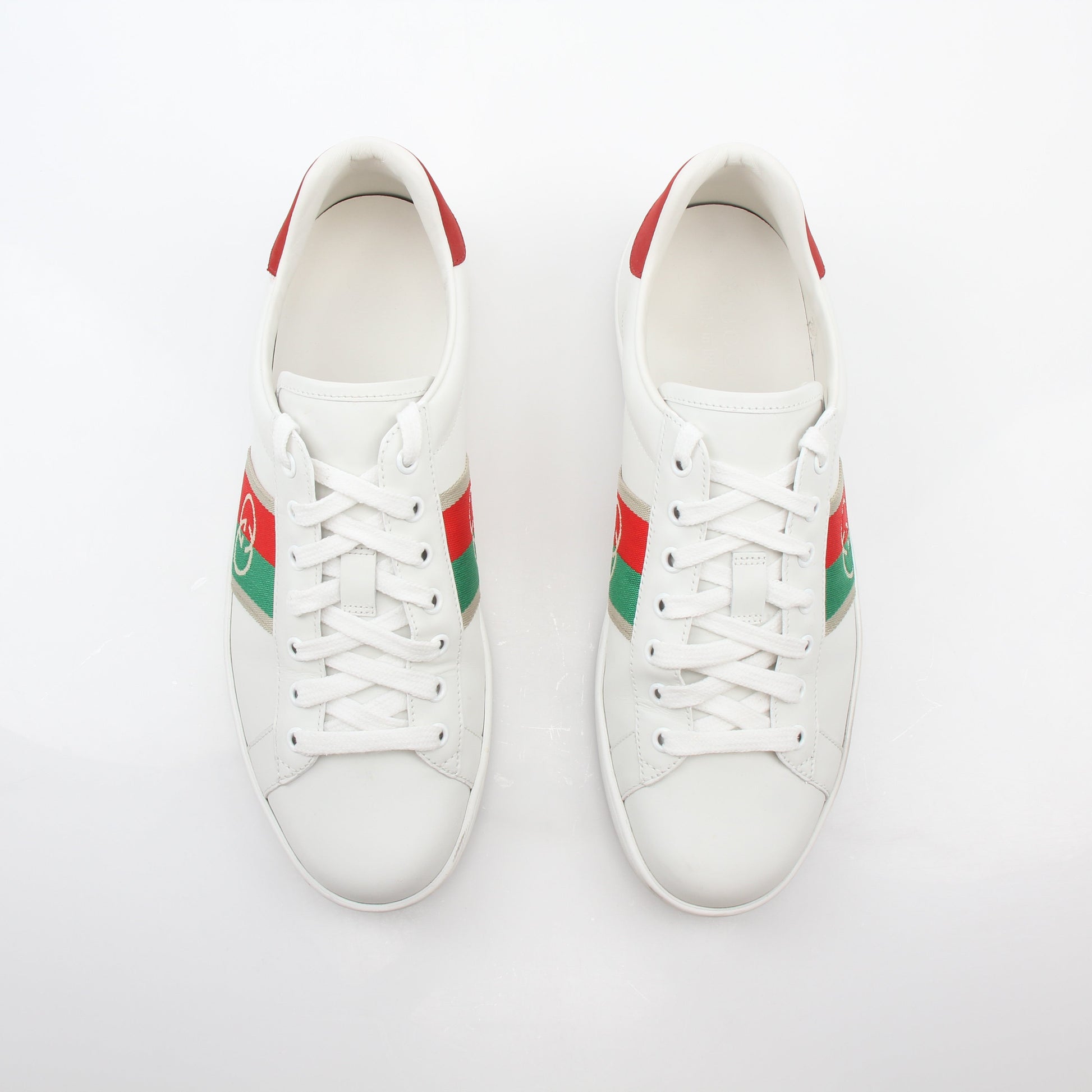 White Gucci Ace sneakers with Interlocking G web leather design, showcasing classic low-top shoes with white laces and branding.
