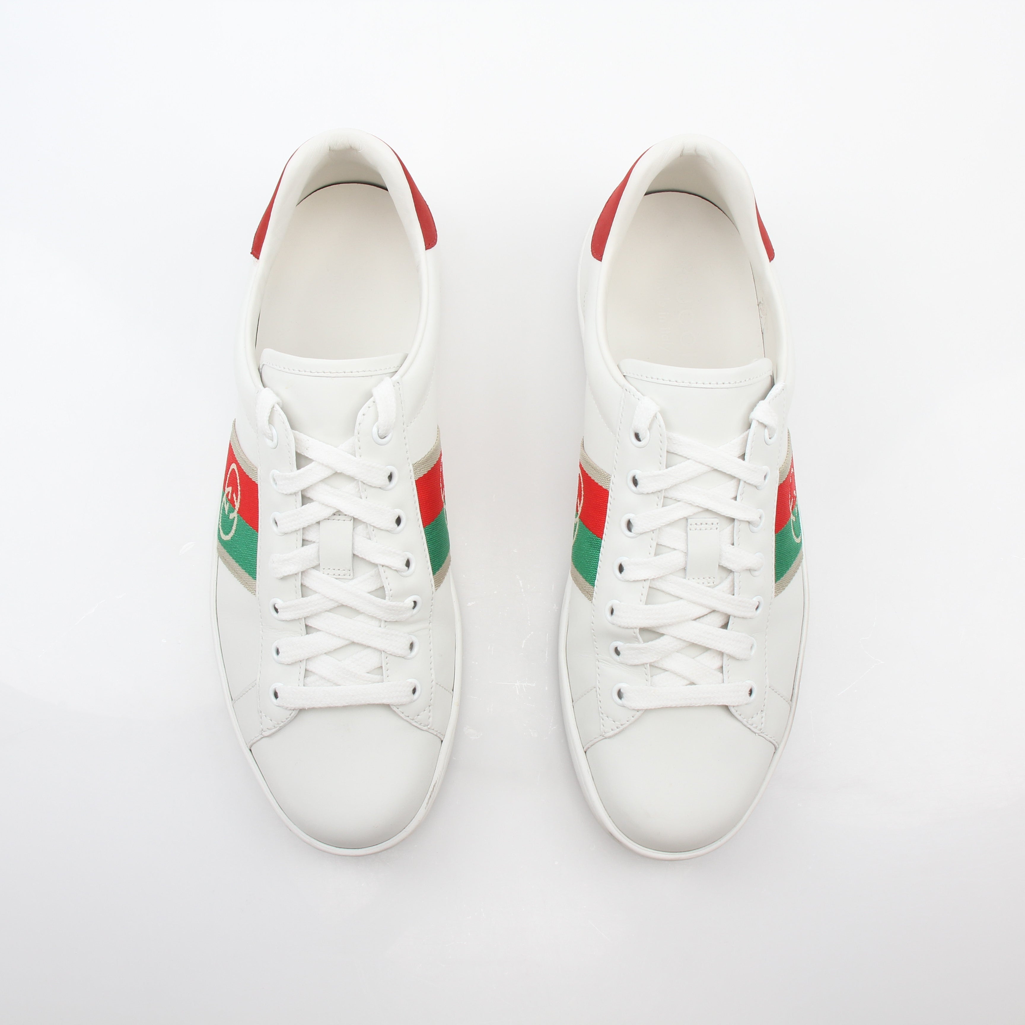White Gucci Ace sneakers with Interlocking G web leather design, showcasing classic low-top shoes with white laces and branding.