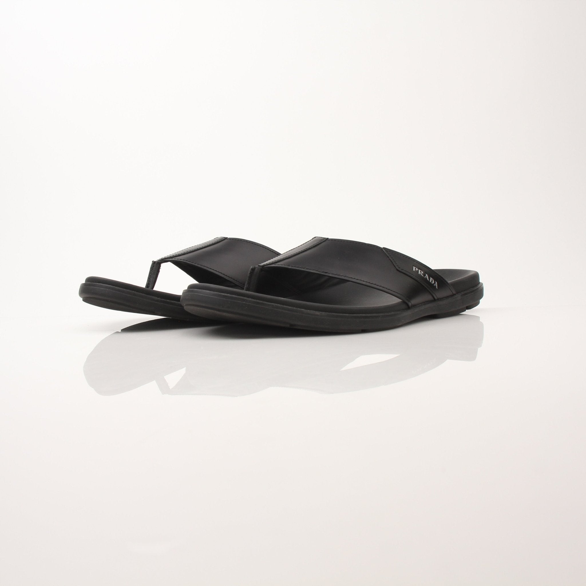 Gold & Beyond men's Prada logo thong sandals, showcasing black leather straps with Prada branding and casual slip-on design.